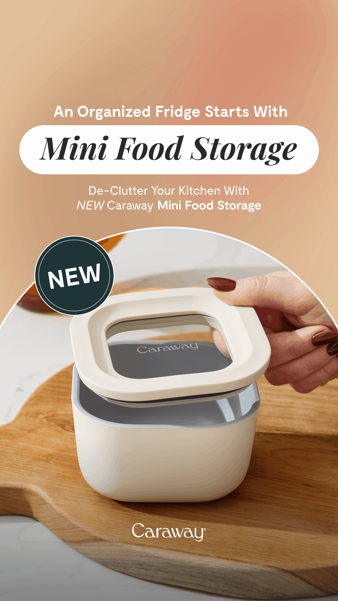 A Caraway mini food storage container with a white square lid, held by a hand with manicured nails, placed on a wooden cutting board.