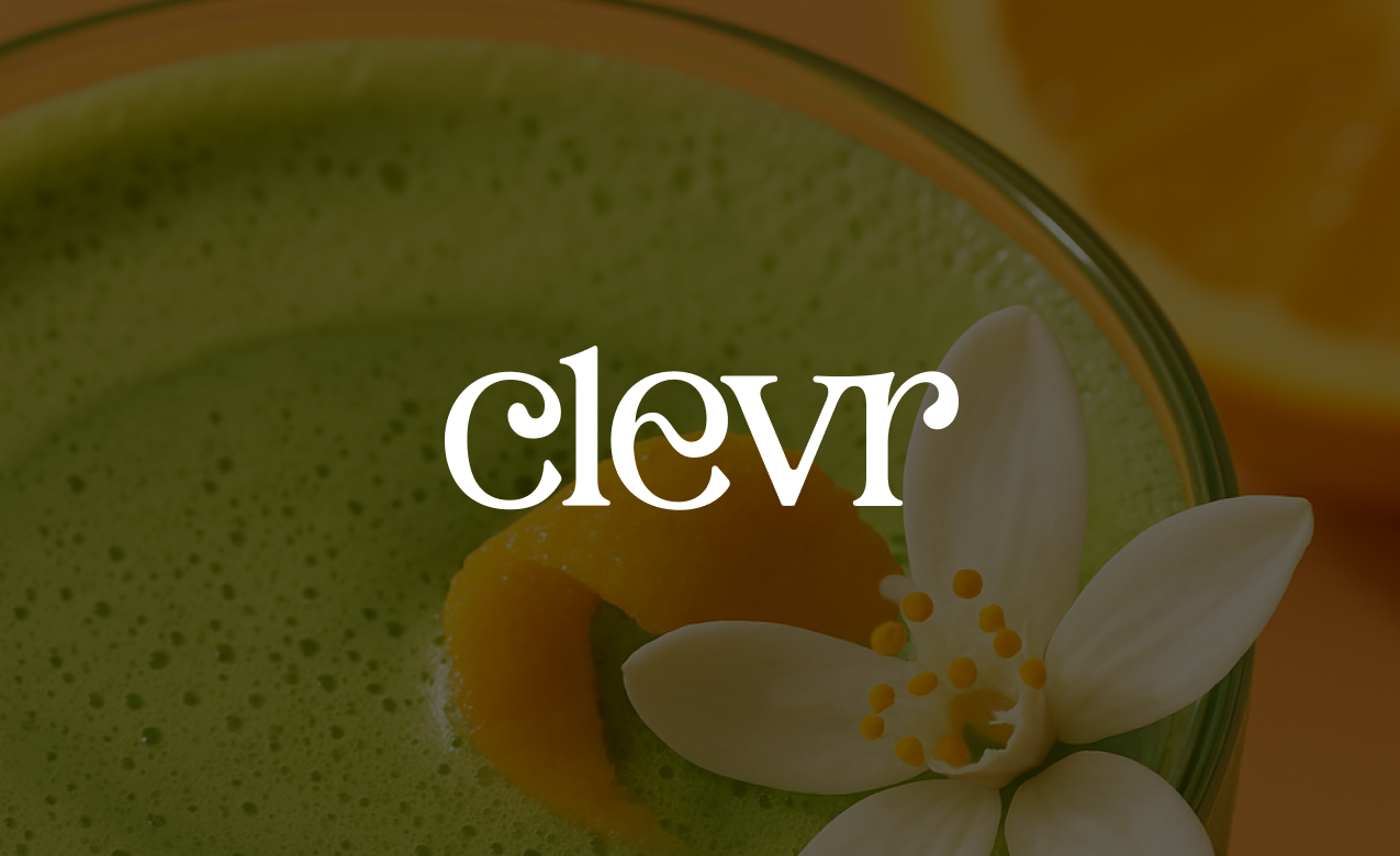 Close-up of a green drink with a white flower and a lime peel garnish in a glass.