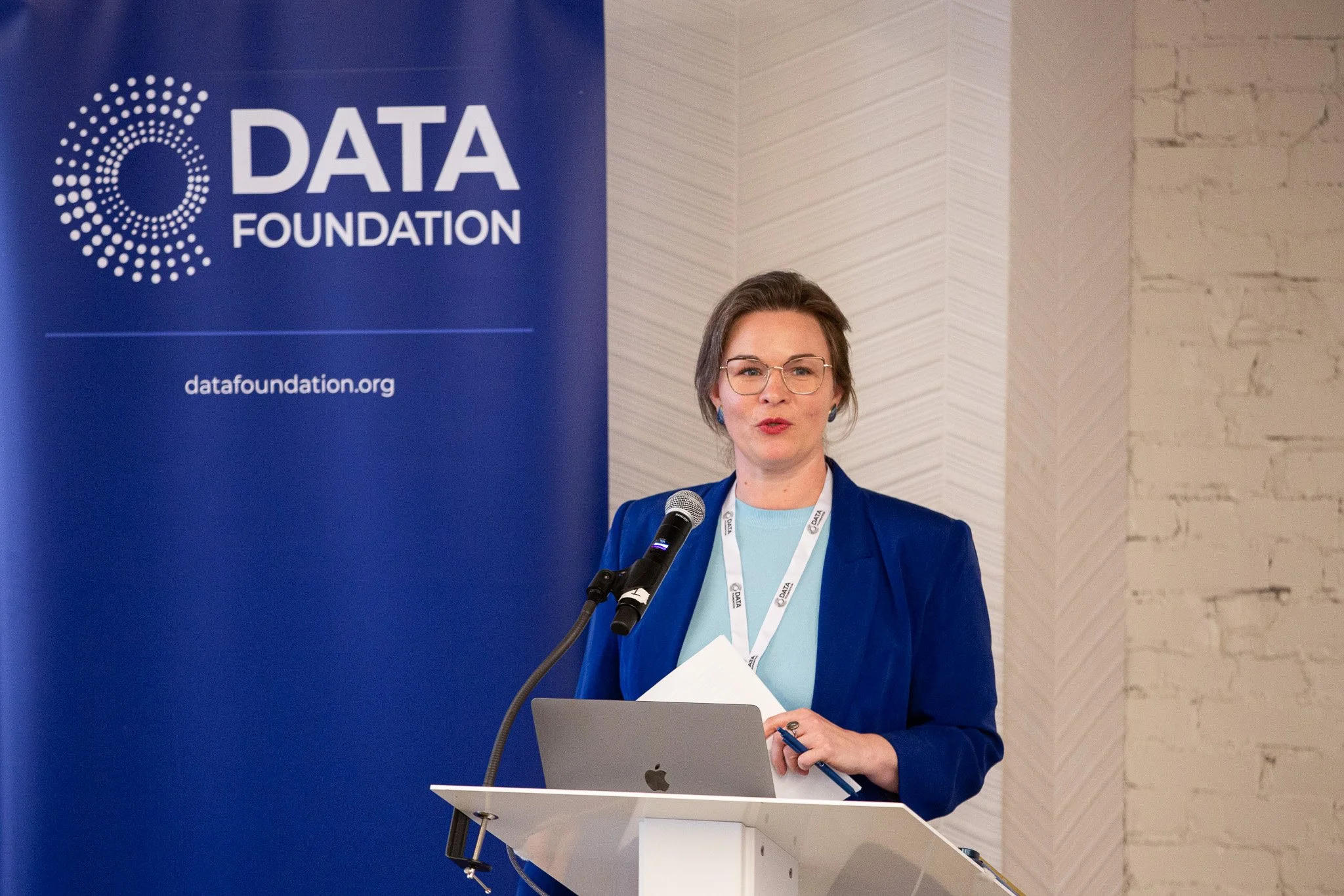 A keynote speaker presents at a Data Foundation conference, addressing attendees from the podium while delivering insights on data, policy, and innovation. Framed by the organization's branding, the image captures the professionalism and engagement o
