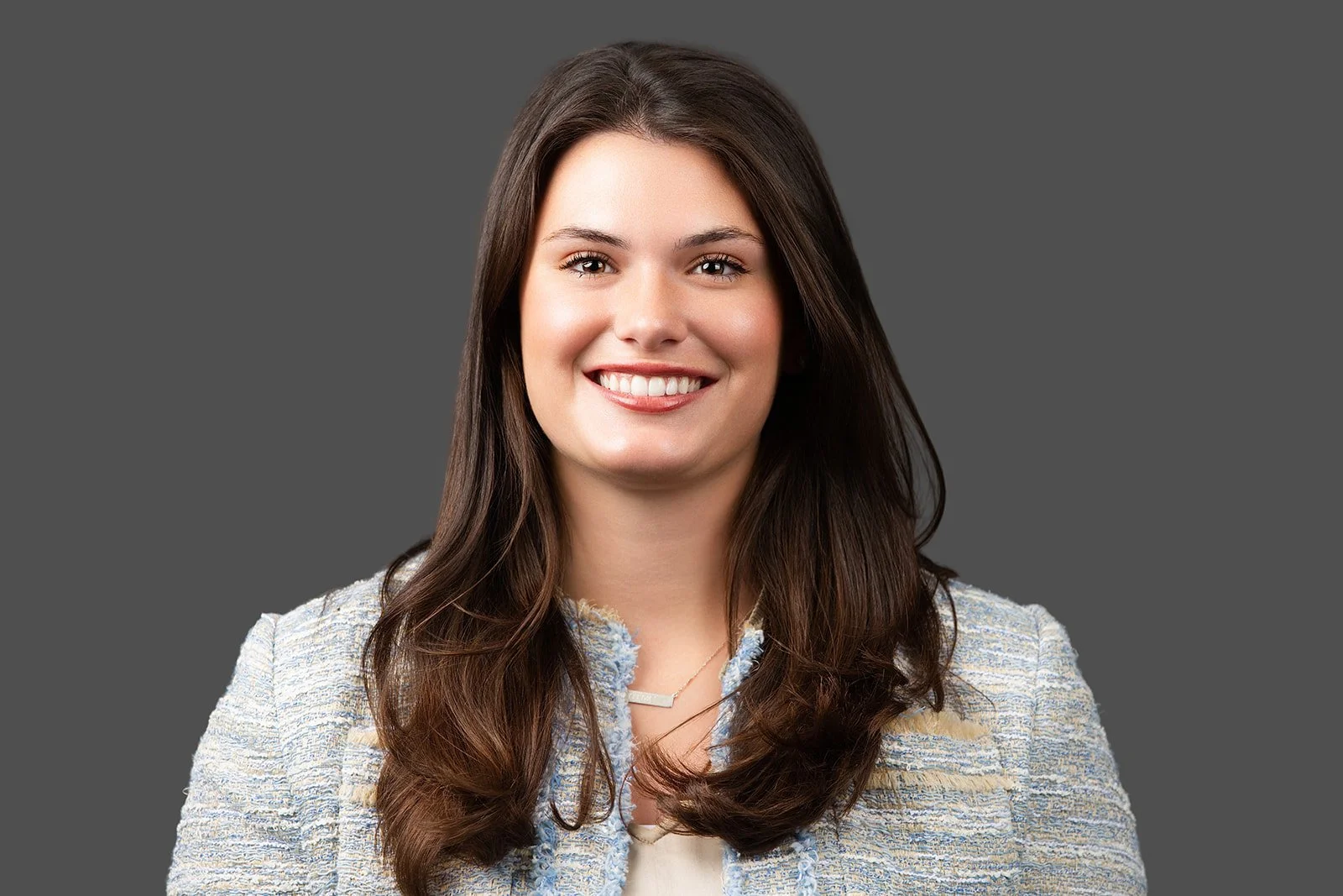 Headshot of a young woman with dark brown medium-length hair, set against a grey background. 