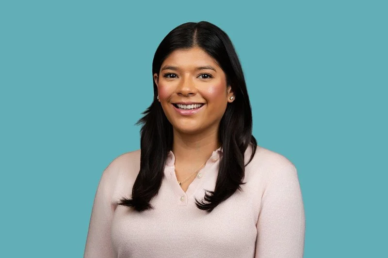 A professional headshot featuring a female business professional in a light-colored blouse against a clean teal background. The portrait captures a confident, approachable presence. 