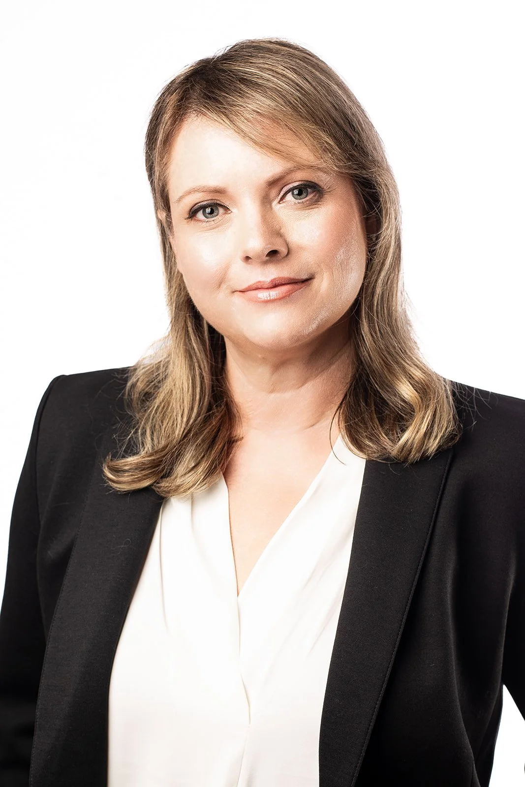 Professional woman with shoulder-length light brown hair, wearing a black blazer and white blouse, smiling softly against a white background.