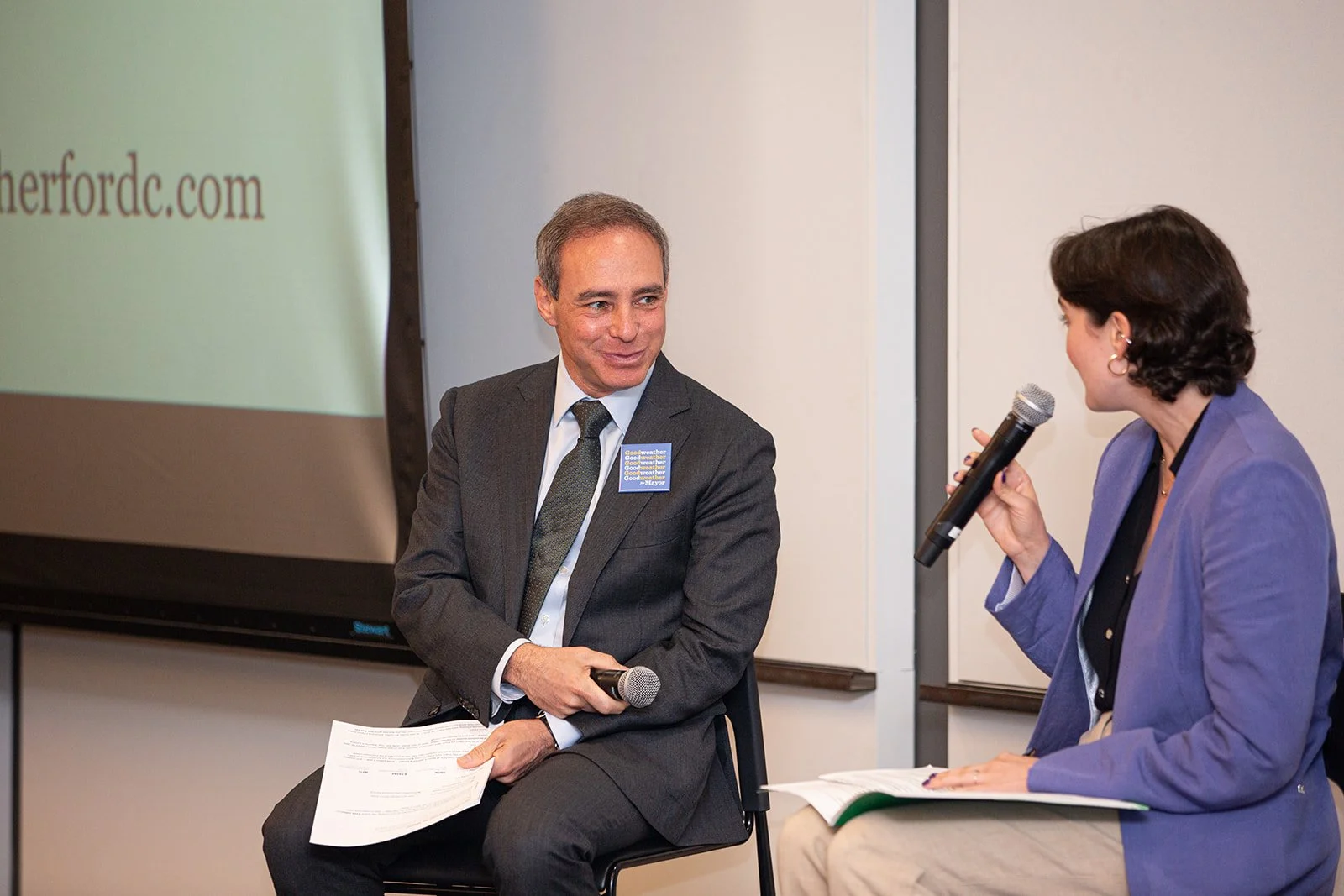 Two people participate in a live interview during a forum, discussing insights on stage with handheld microphones. Photographed by a Washington DC photographer.