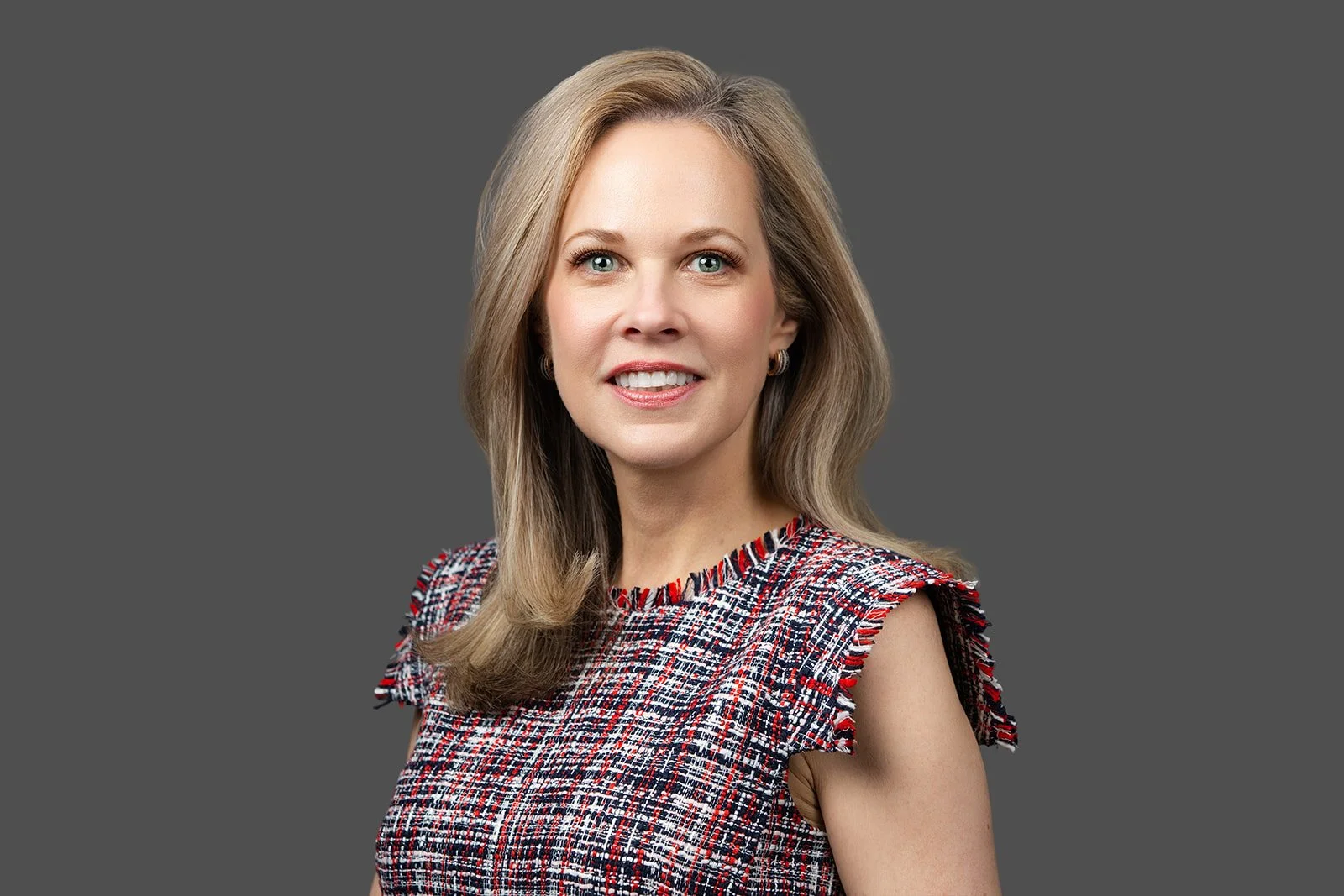 Headshot of a middle-aged woman with blonde medium-length hair, smiling against a grey backdrop.
