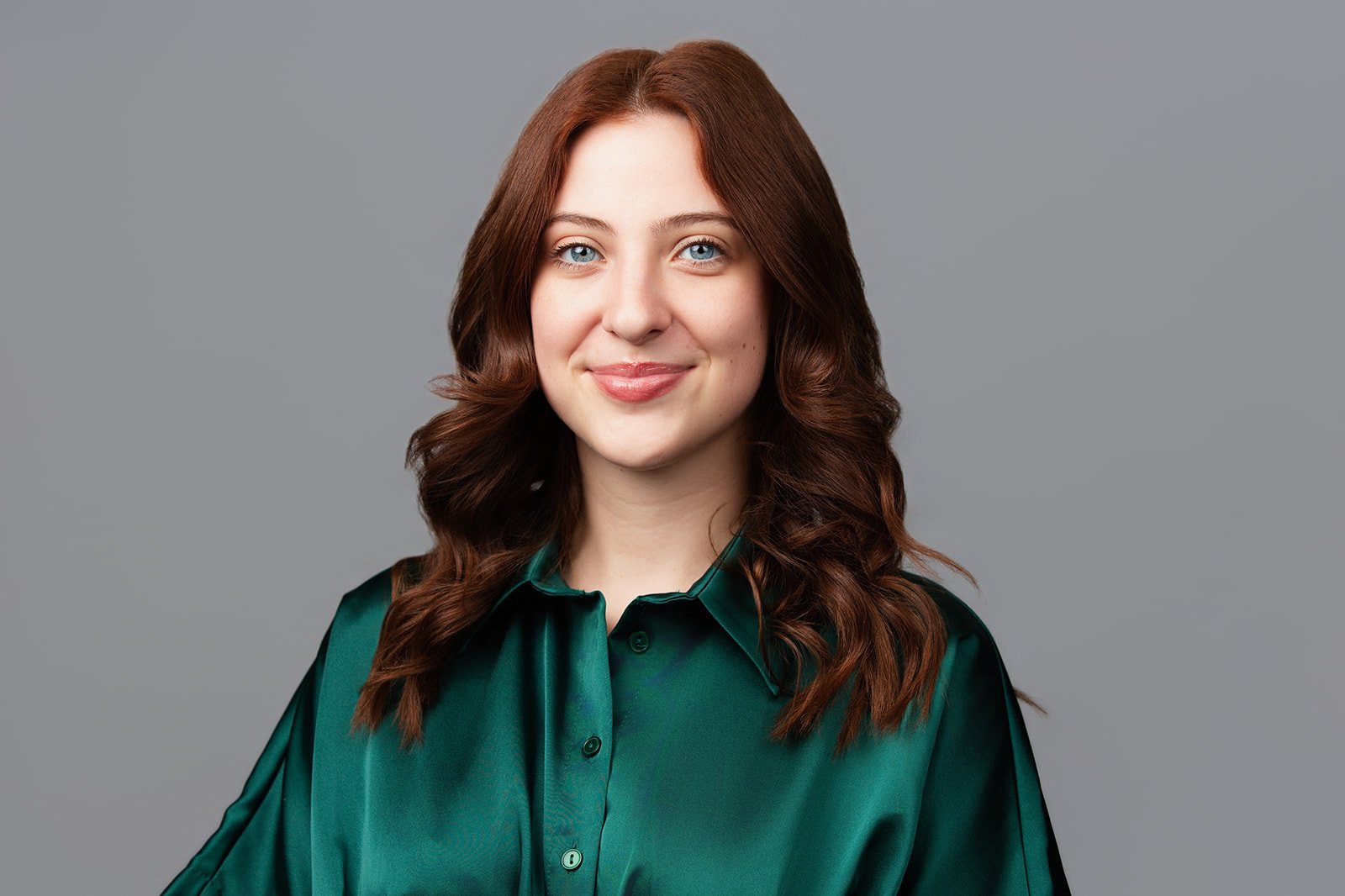 Professional corporate headshot of a woman with brown hair wearing a green blouse against a neutral gray background.