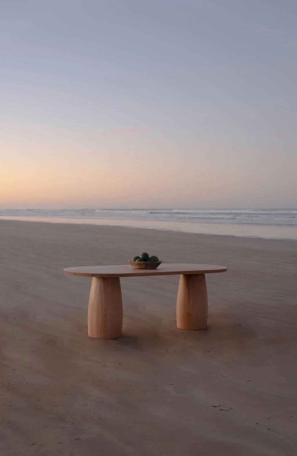 A contemporary hand-crafted timber dining table on a beach at sunset