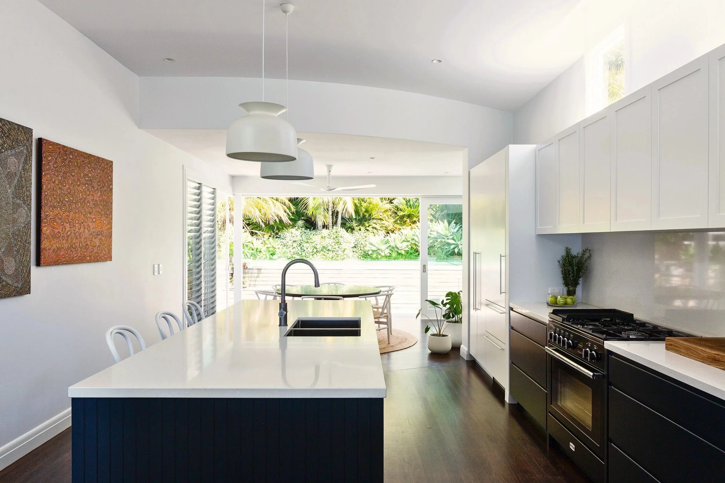 Modern kitchen with white island, black cabinetry, stainless steel oven, white upper cabinets, and outdoor patio with garden view.