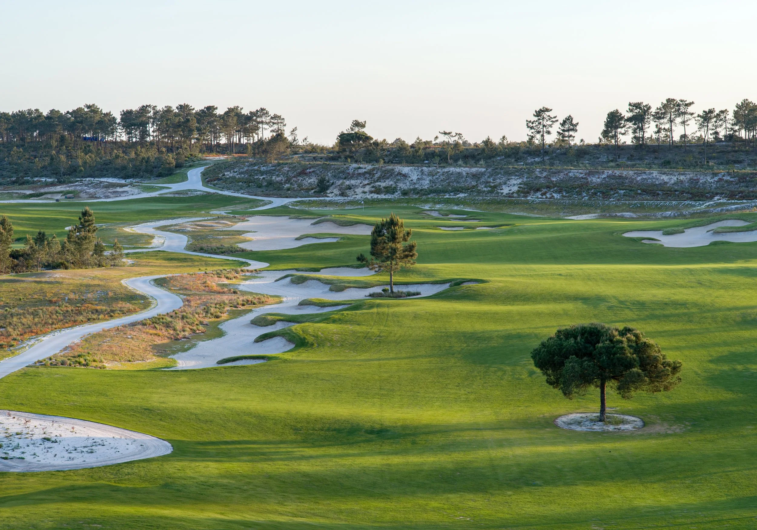 A golf course with lush green fairways, sand bunkers, and a winding water hazard surrounded by trees and rolling hills.