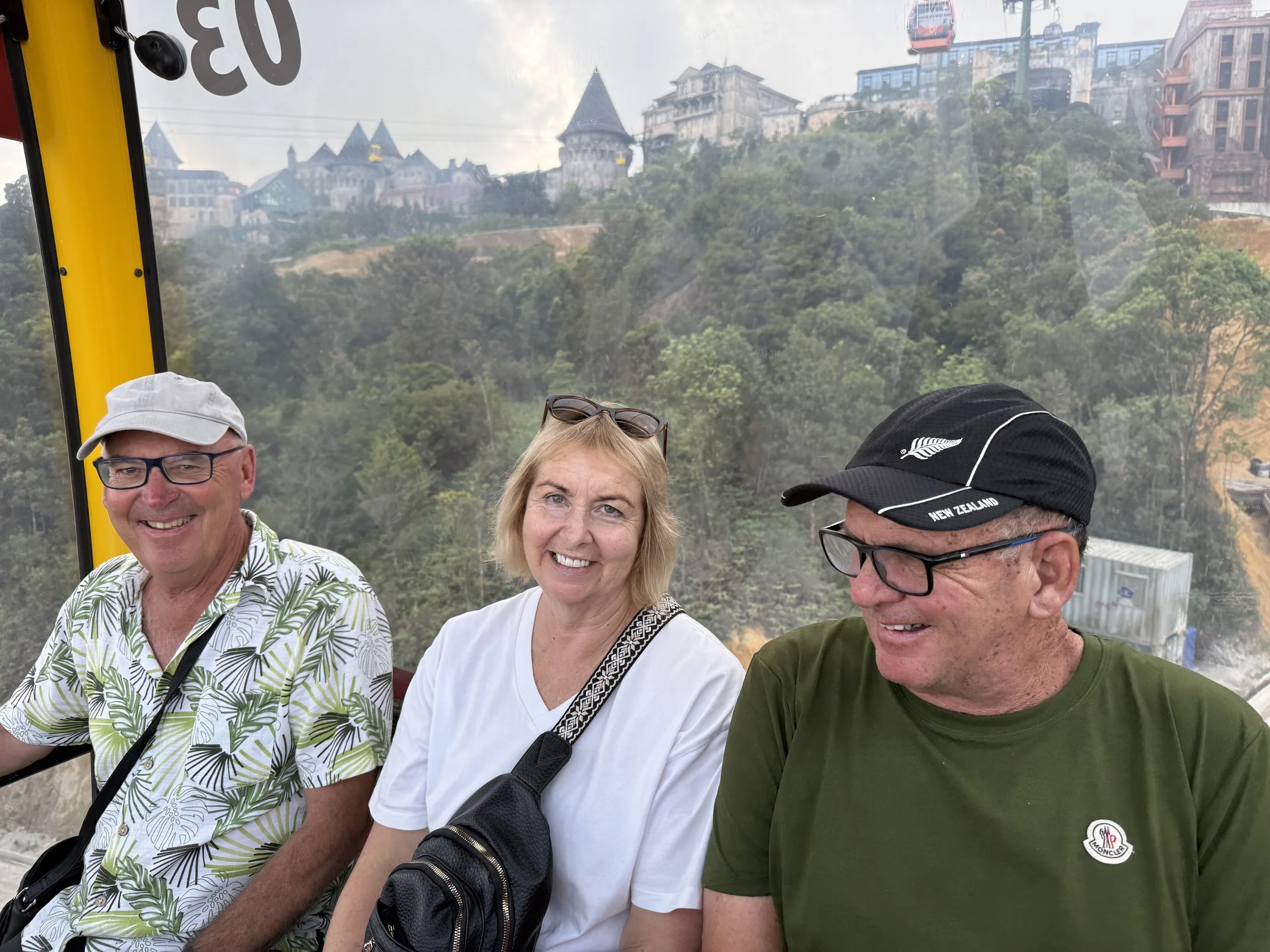 Four people sitting inside a cable car with a scenic cityscape and hilly terrain visible through the window behind them.