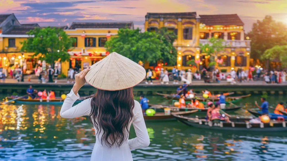A woman wearing a traditional Vietnam conical hat in Hoi An, Da Nang, Vietnam with boats and Vietnamese lanterns, seen on a hosted Vietnam golf tour with the 19th Golf Escapes.