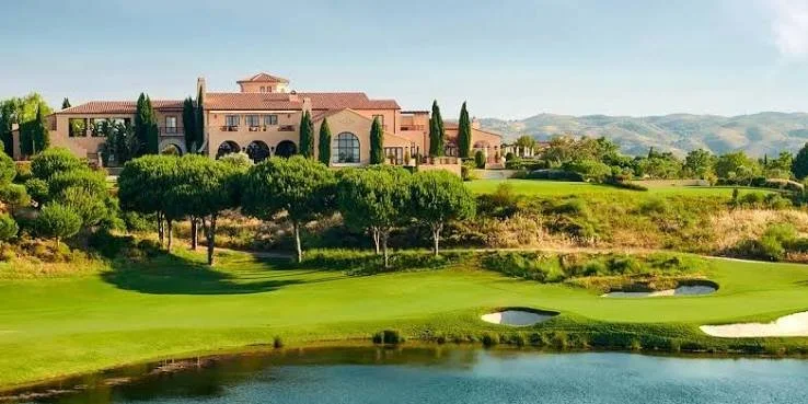 Luxury mansion with a golf course, water features, and scenic hills in the background.