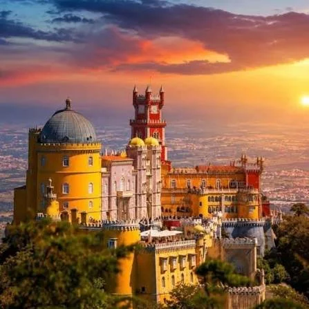 Colorful castle with yellow, pink, and red towers at sunset, overlooking a cityscape.