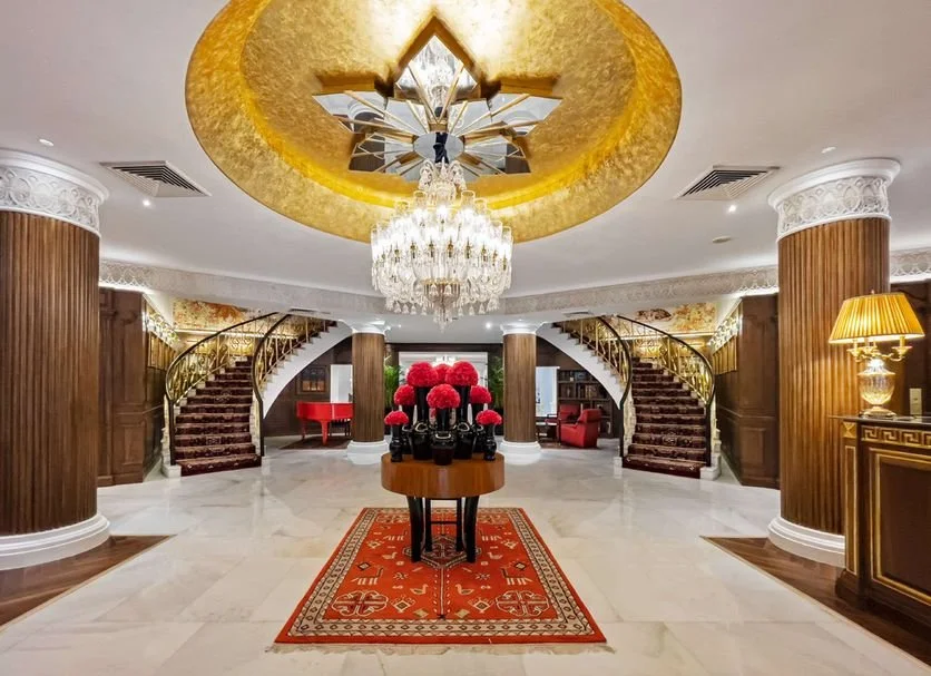 Luxurious hotel lobby with a chandelier, grand staircase, and floral arrangement.