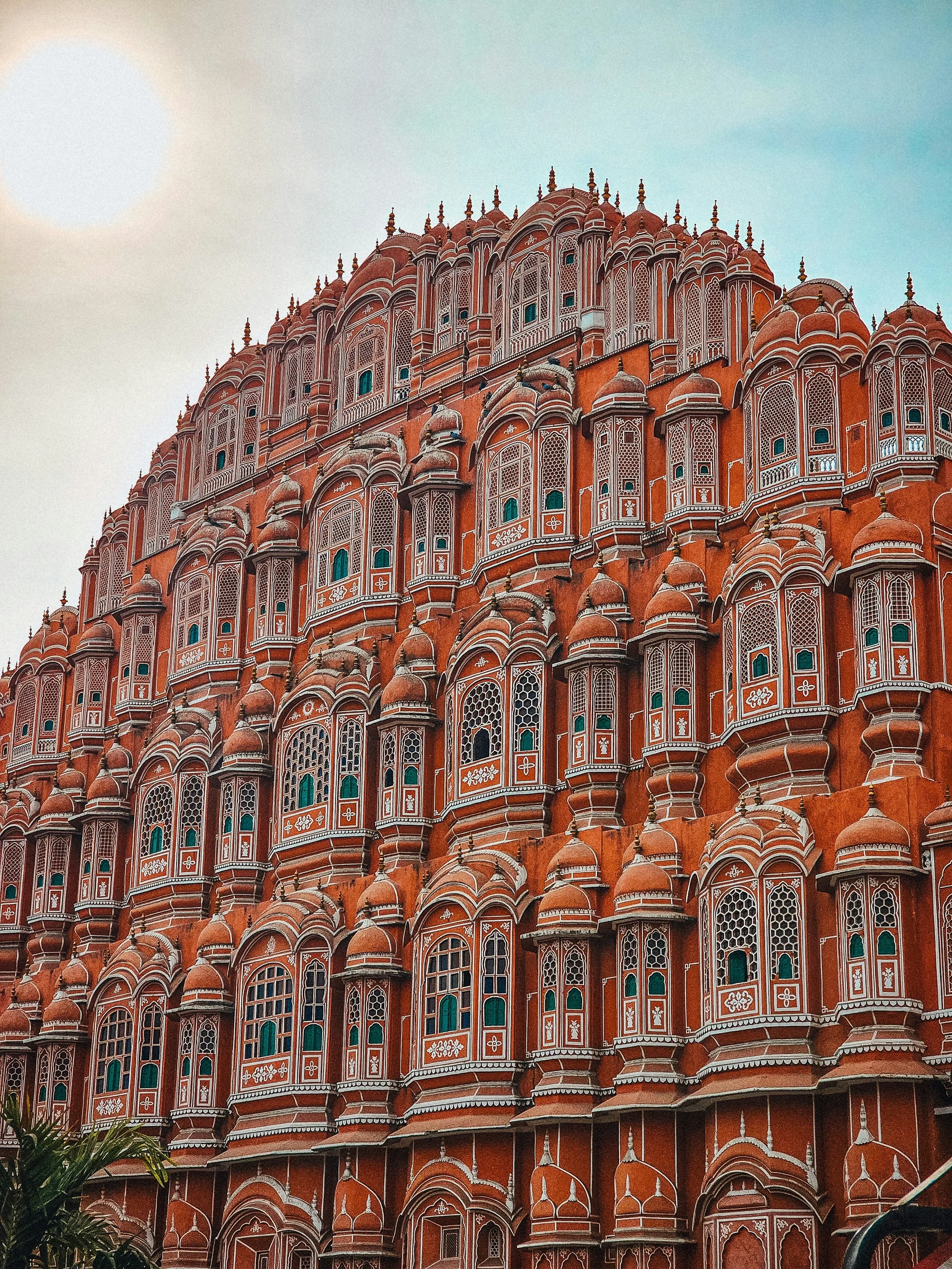 The image shows a large, red sandstone building with intricate white carvings and multiple small domes and windows, which appears to be a historical palace or fort, likely in India.