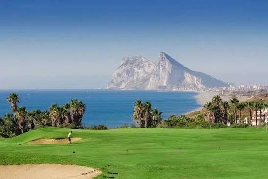 Golf course with a player near the green, palm trees, and a large mountain or island in the background by the ocean.