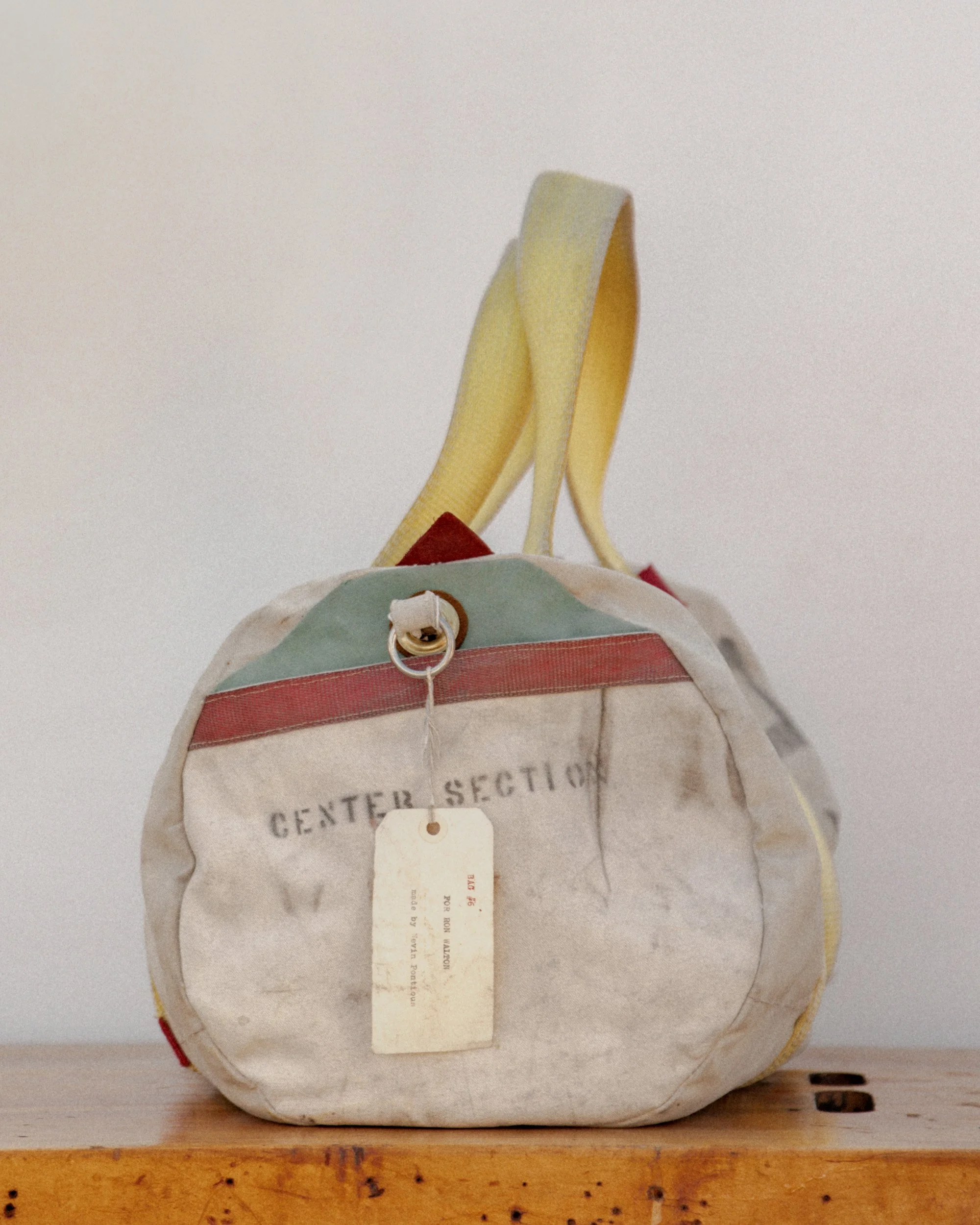 A vintage, worn fabric bag with handles, labeled 'CENTER SECTION', sitting on a wooden surface against a plain wall.