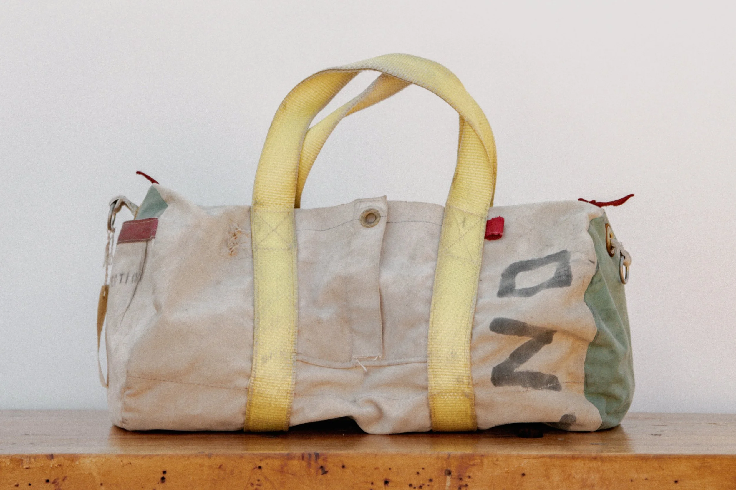 Worn, dirty duffel bag with yellow handles on a wooden surface.