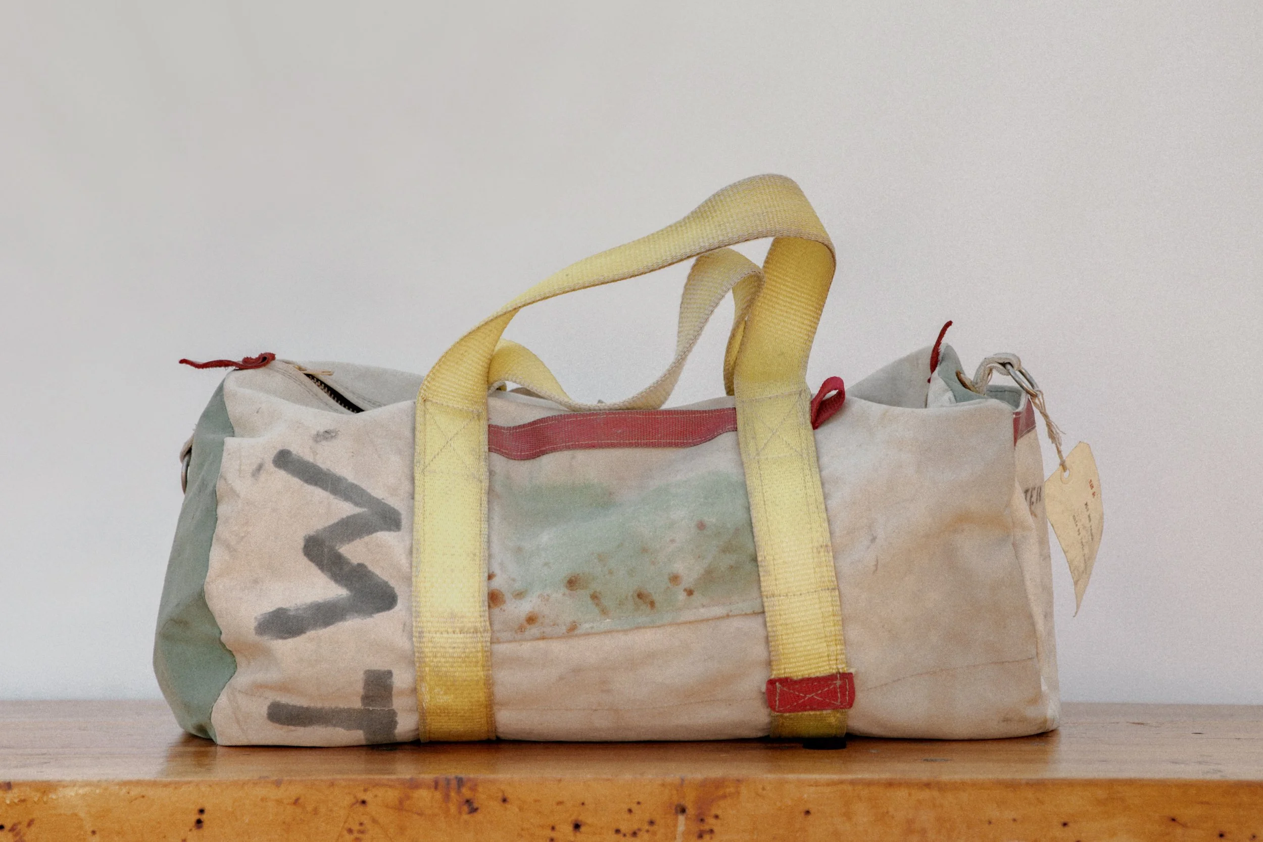 A used, dirty duffel bag with yellow straps resting on a wooden surface.