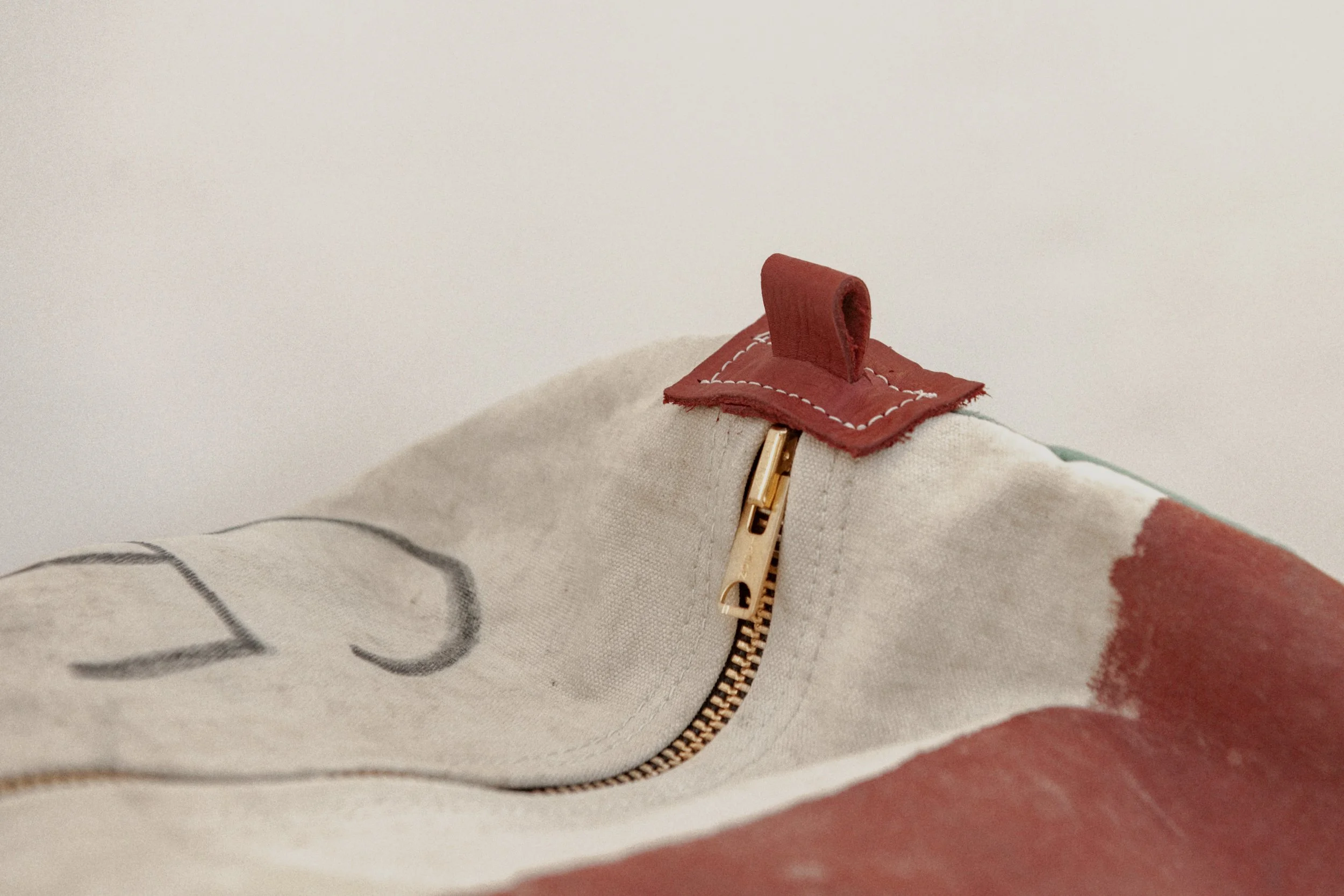 Close-up of a fabric bag with a gold zipper and a red leather pull tab.