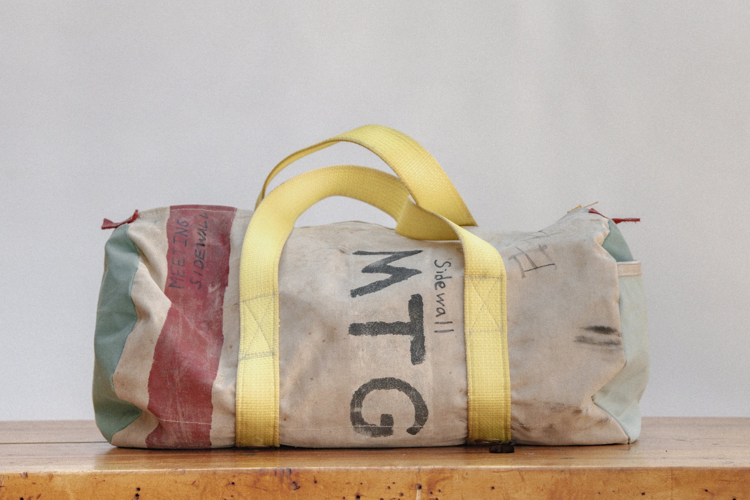 A worn fabric bag with yellow handles and multicolored sections is placed on a wooden surface. The bag has handwritten text, including 'GTM' and other markings.