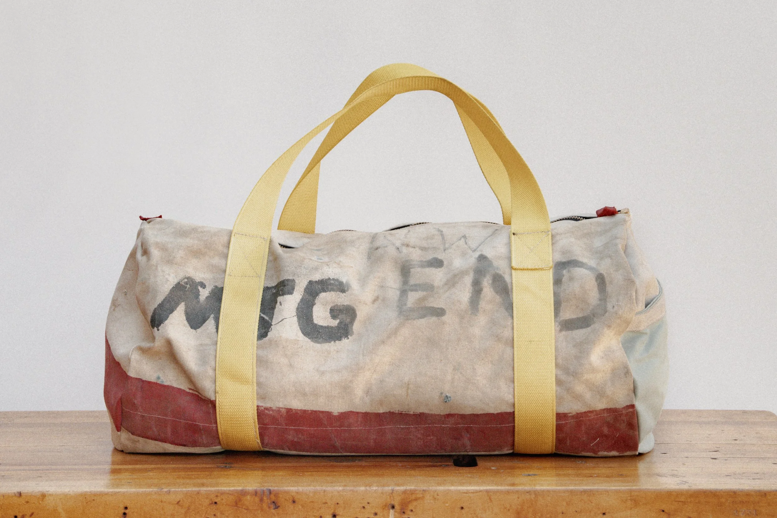 A well-worn duffel bag with yellow straps, resting on a wooden surface, with faded and stained fabric that says MEETING END