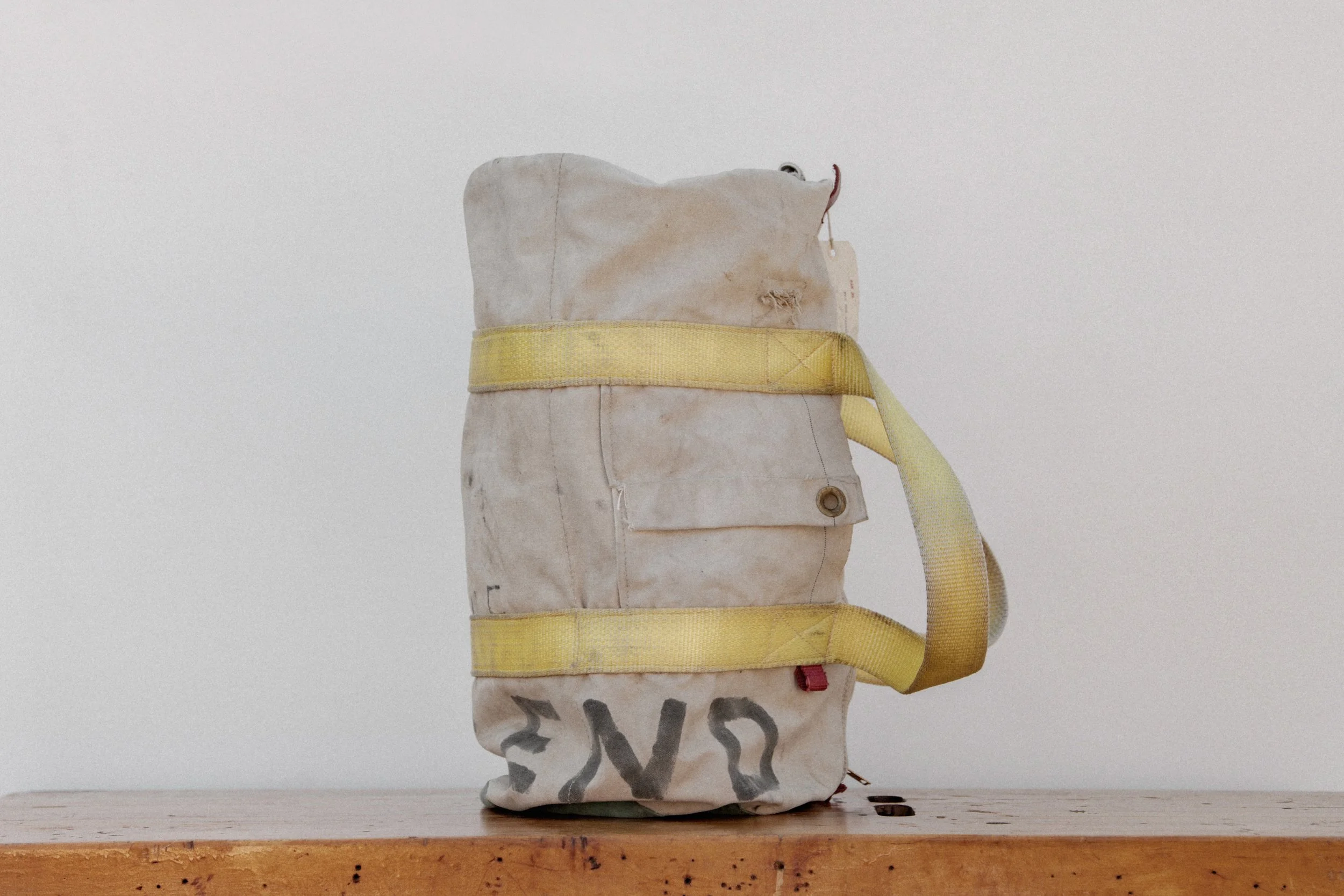 Old, worn-out backpack with yellow straps on a wooden surface against a plain white background.
