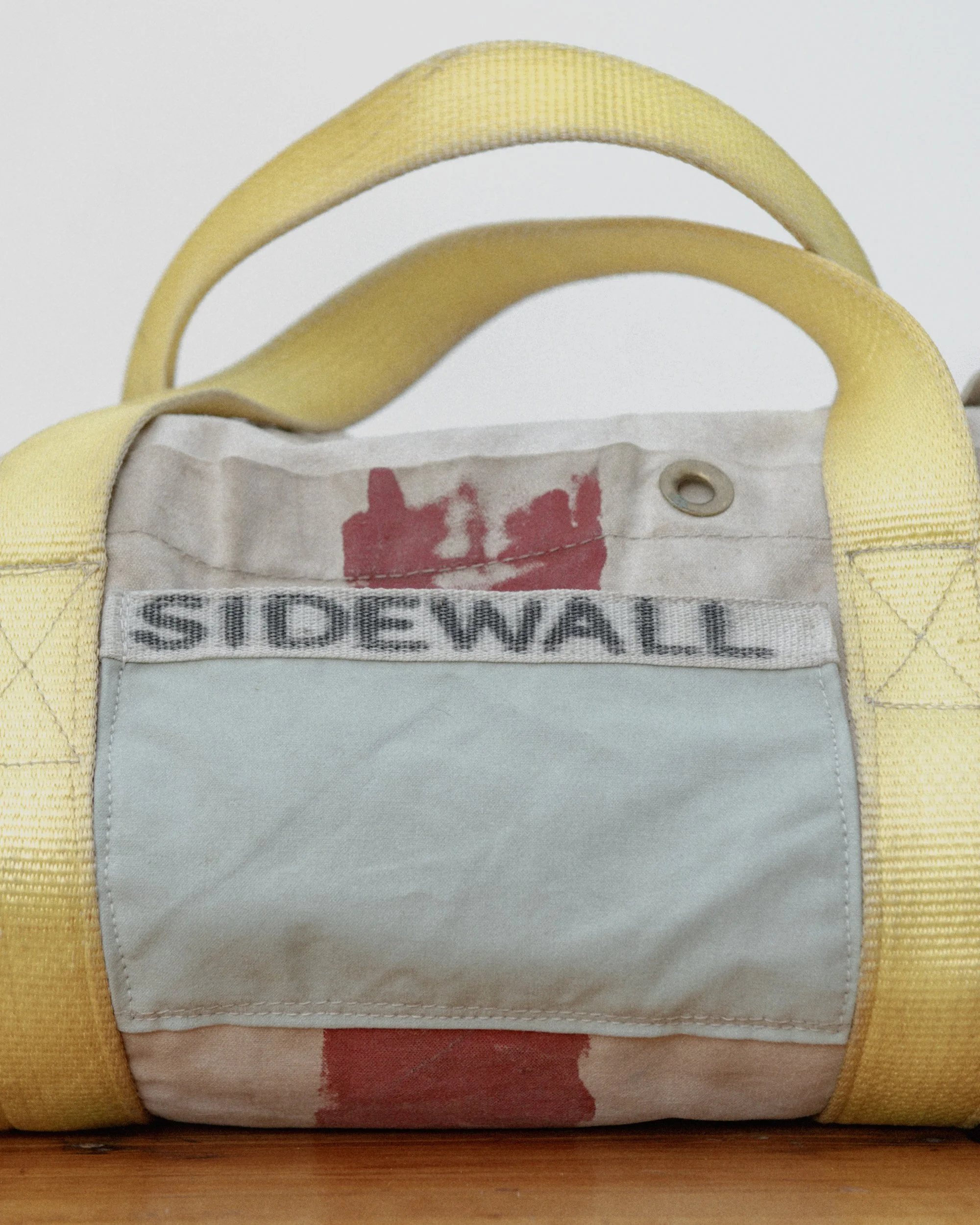 Close-up of a yellow and beige fabric bag with a white label that says 'SIDEWALL' and a partially visible red graphic or text inside.