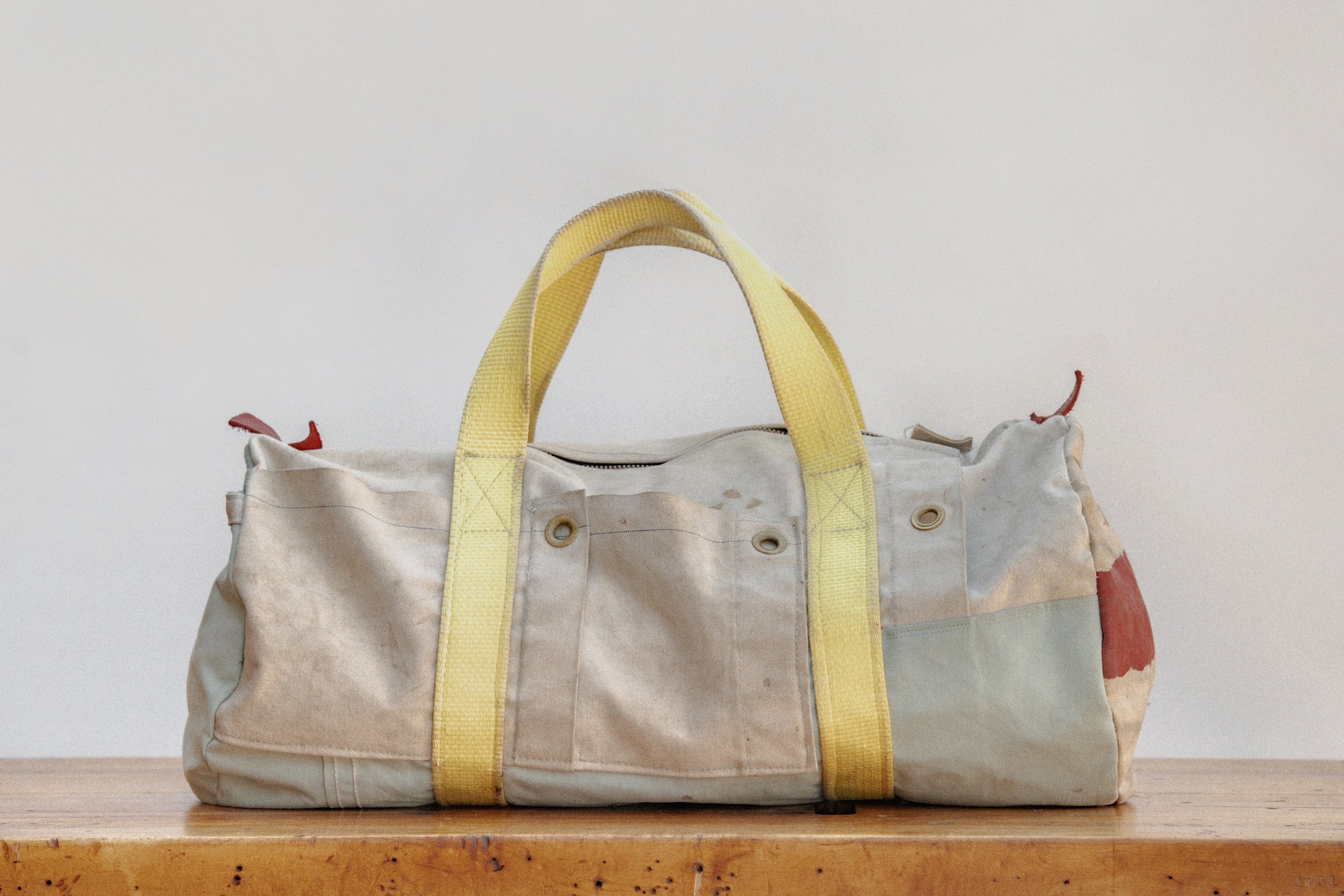 Old, stained fabric duffel bag with yellow handles sitting on a wooden surface.