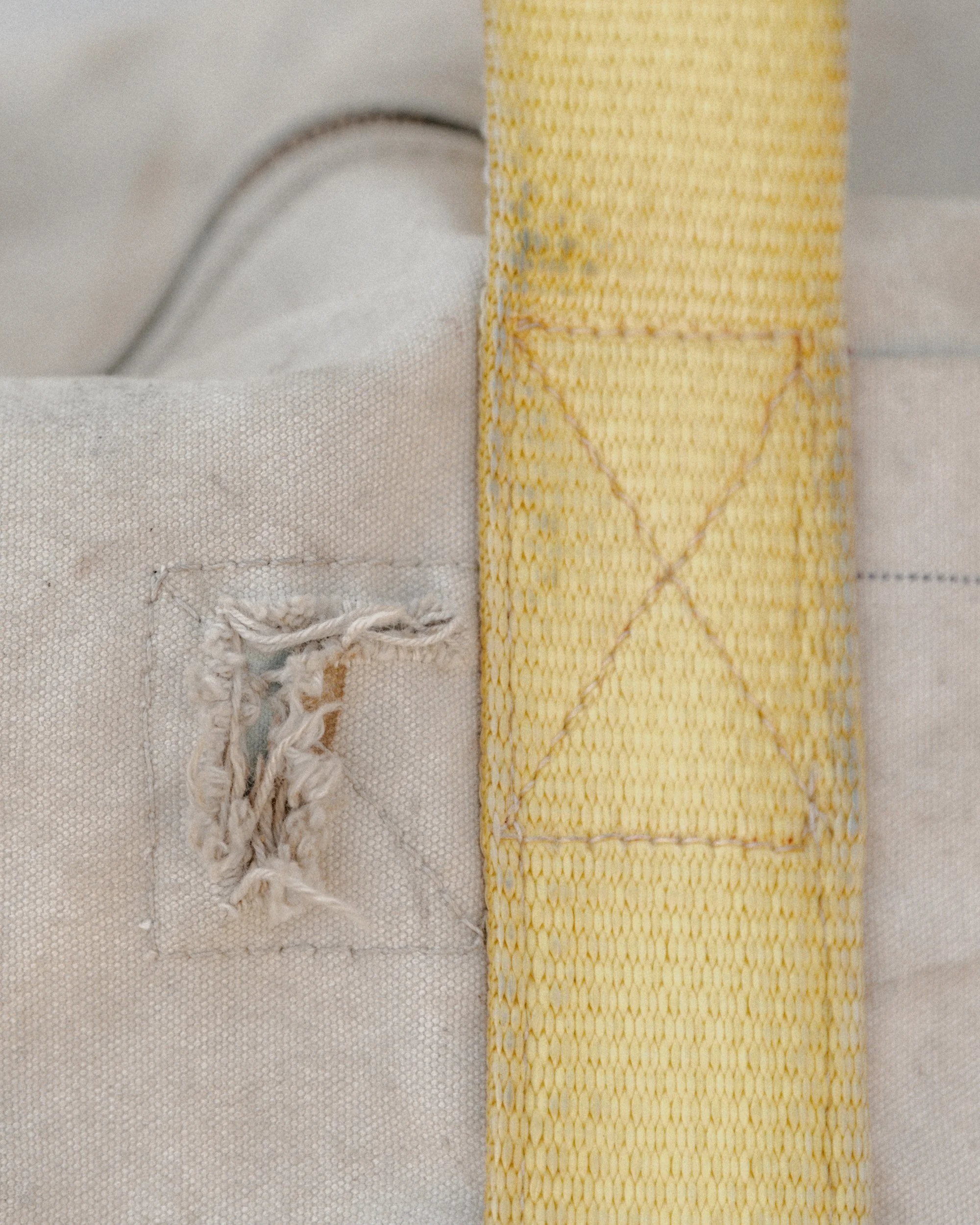 Close-up of a torn, frayed fabric patch on a light-colored textile next to a yellow woven strap.