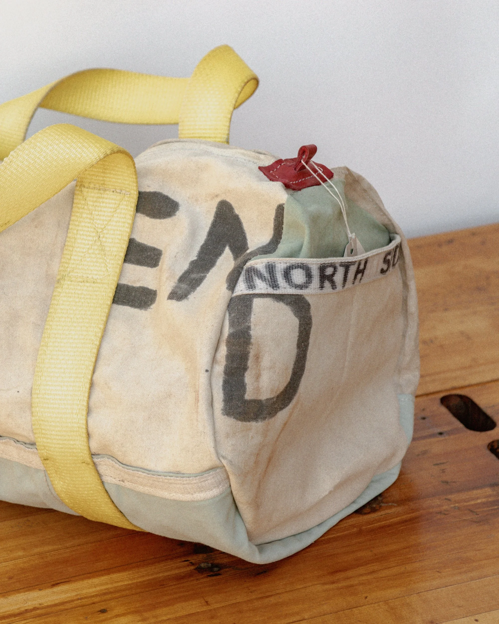 A vintage canvas tote bag with yellow straps resting on a wooden surface.