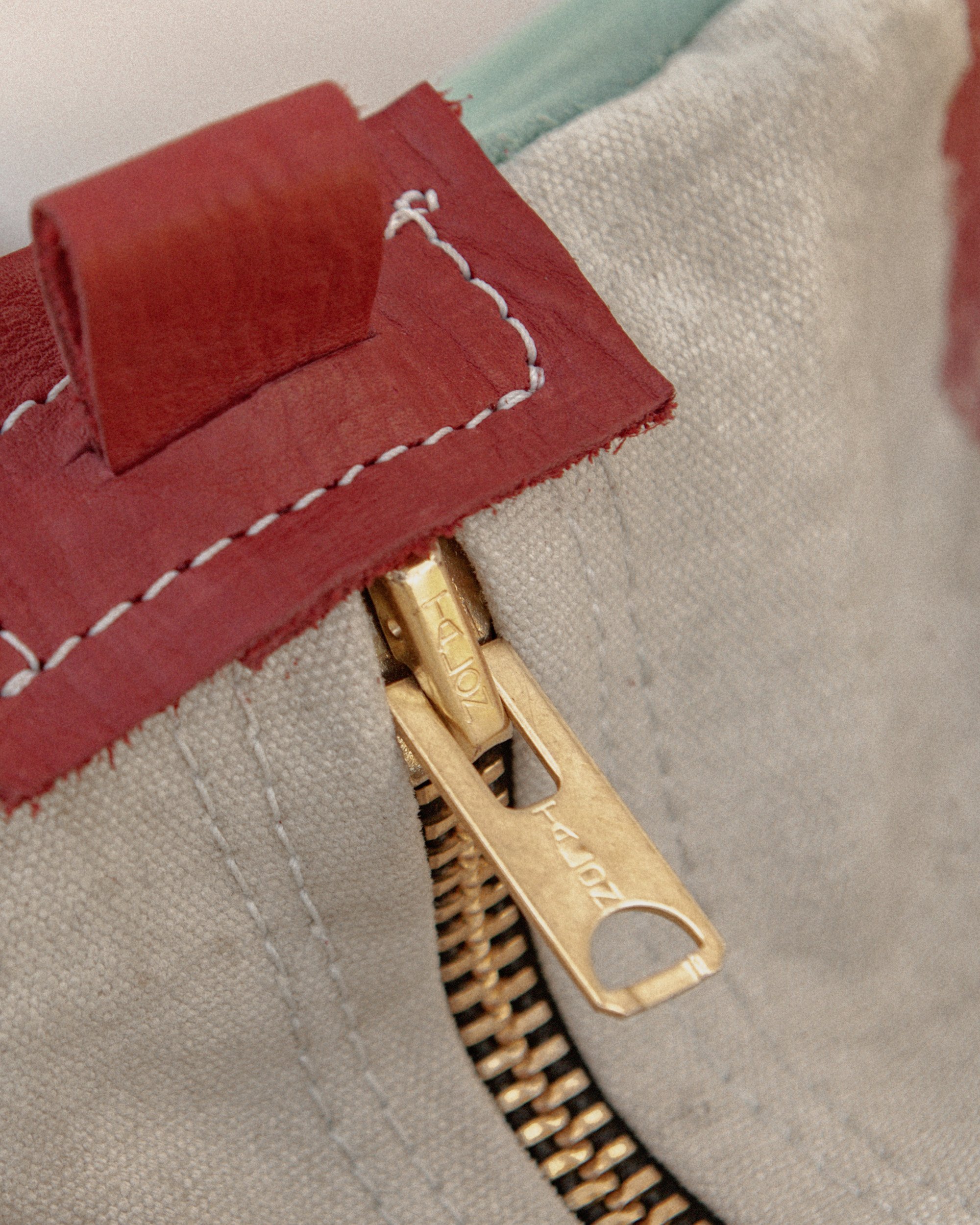 Close-up of a gold zipper on beige fabric with red and mint green leather accents.