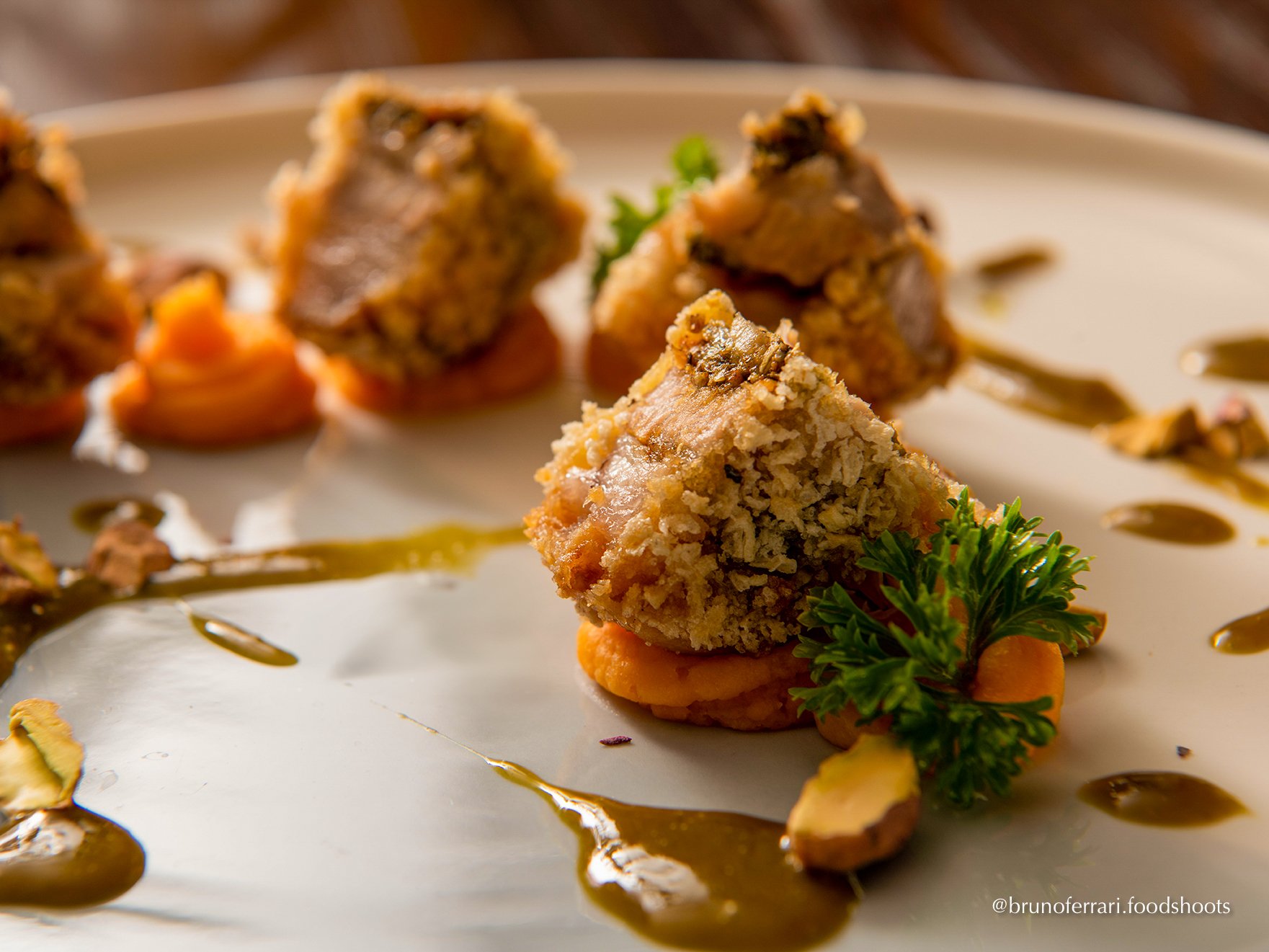 Close-up of breaded meatloaf pieces with garnish and sauce on a white plate.