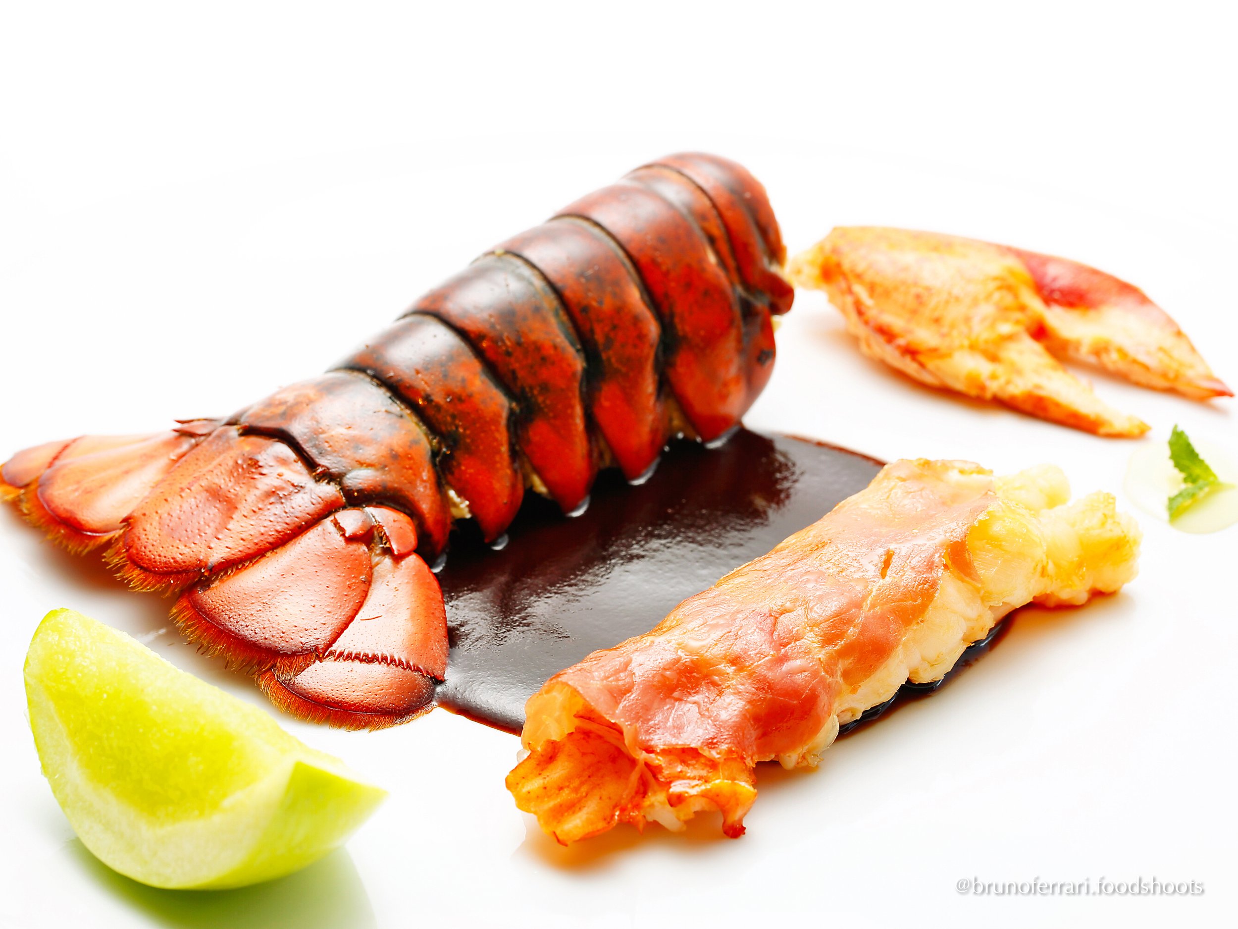 Lobster tail with sauce, lemon wedge, and garnishes on a white background.