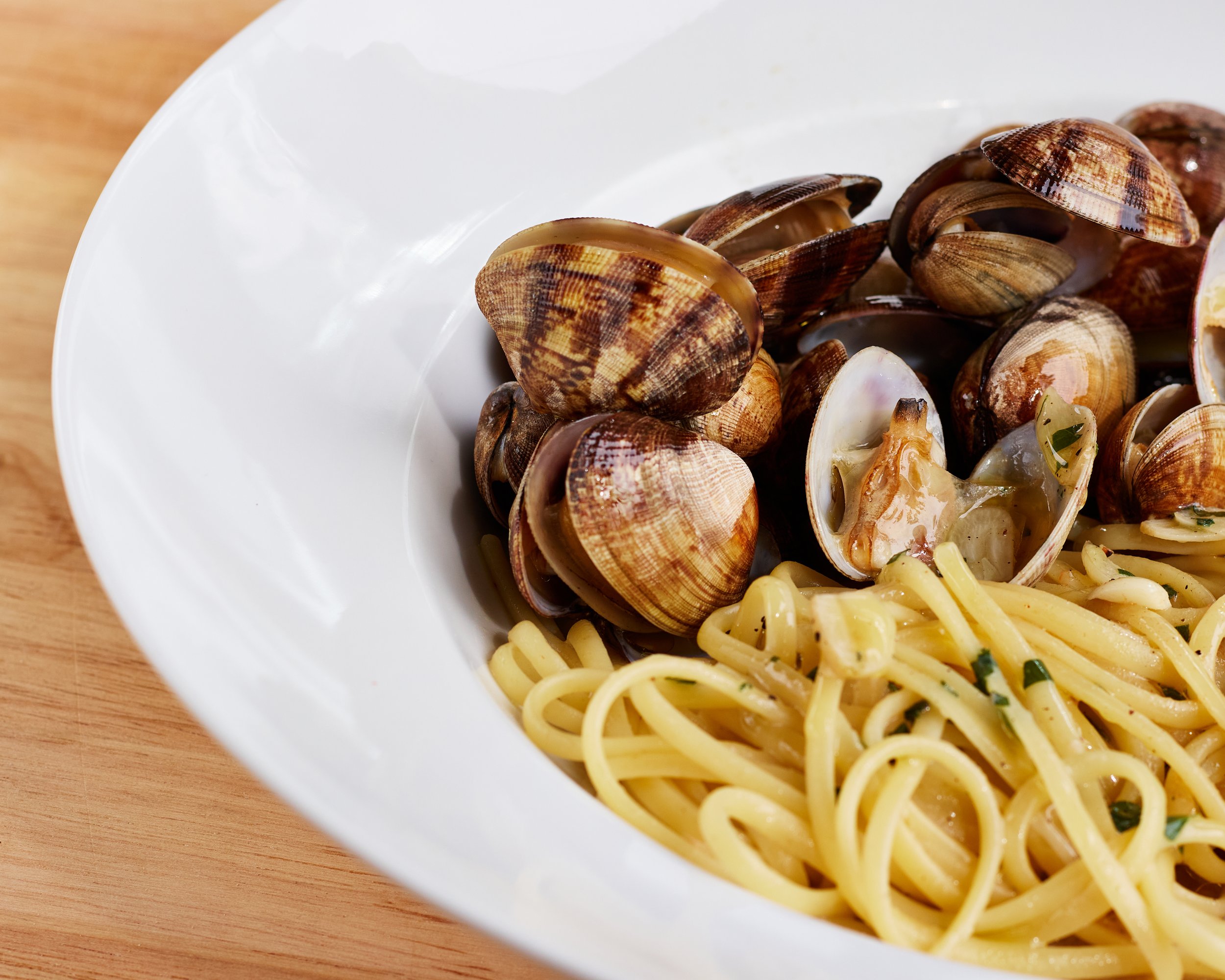 A white bowl of spaghetti pasta with clams on a wooden surface. linguini pasta clams, aglio e olio, peperoncinio