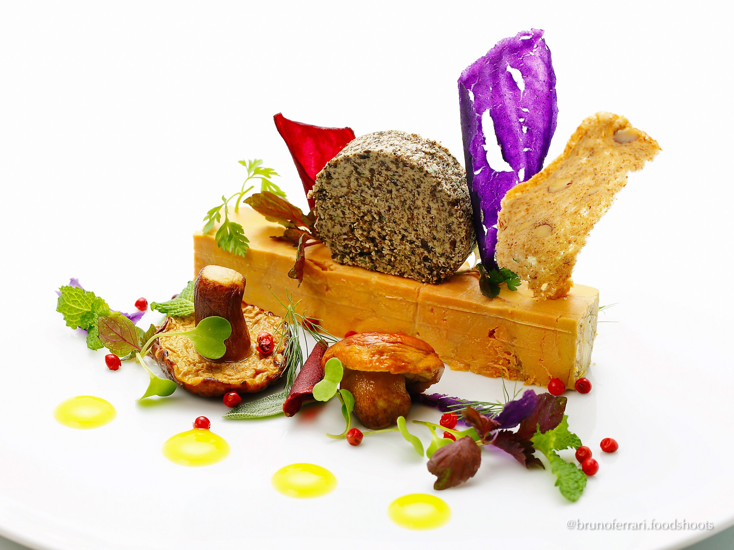 Gourmet cheese platter with assorted cheeses, microgreens, edible flowers, purple and beige cracker chips, roasted mushroom, and small drops of yellow oil on a white plate.