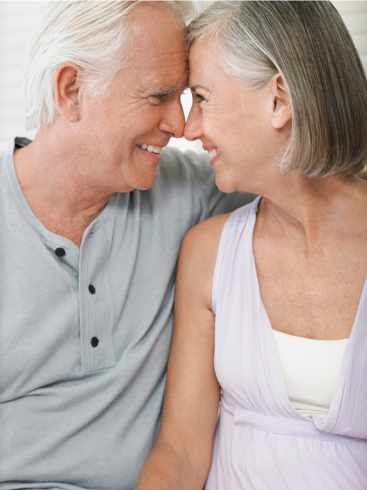 An elderly couple with gray hair smiling and touching foreheads, showing affection.