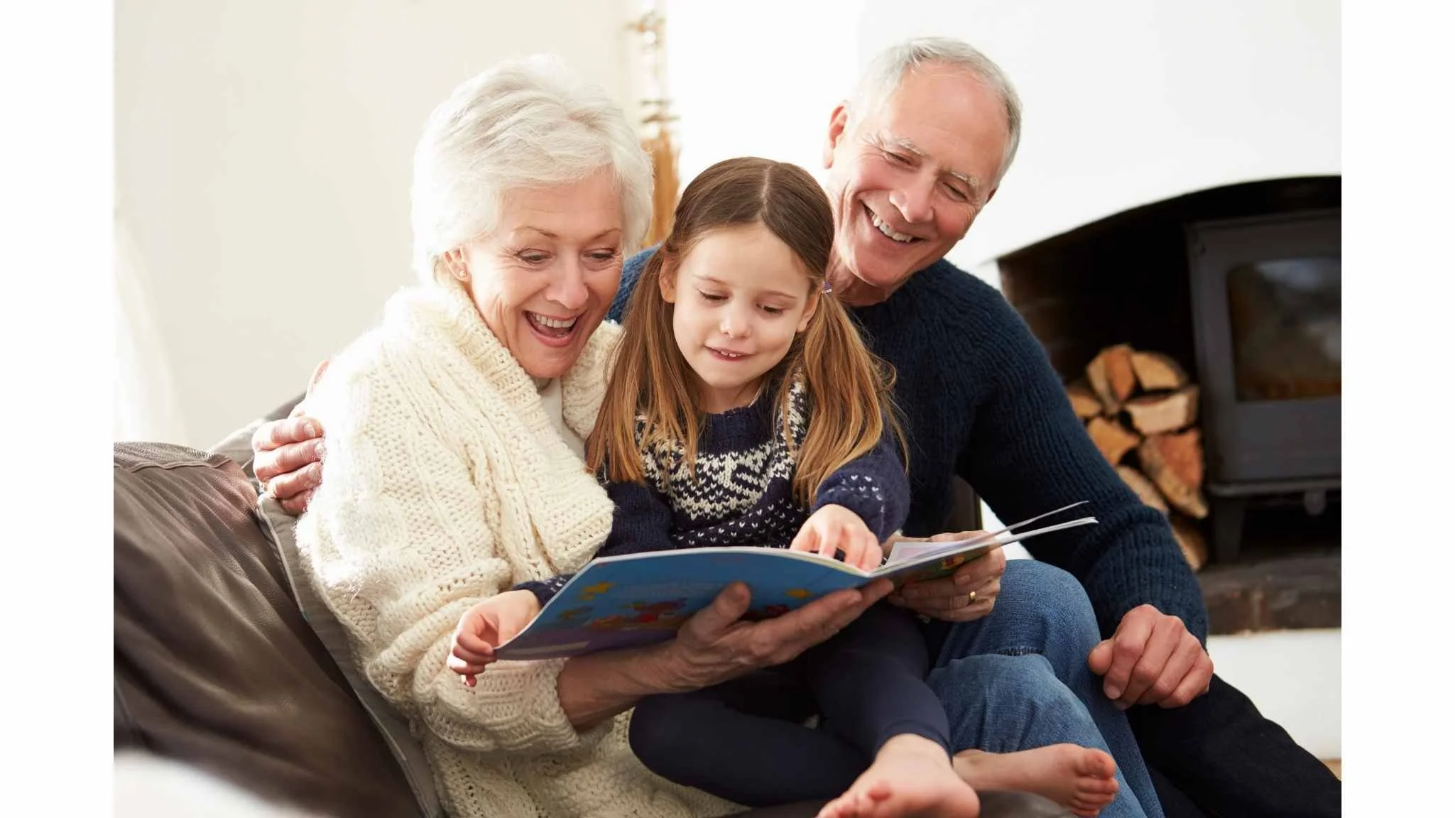 Grandparents and granddaughter reading a book together on a couch in a cozy living room.