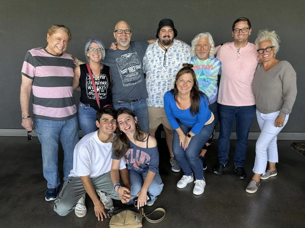 Group of ten people posing together indoors against a dark gray background, smiling at the camera.