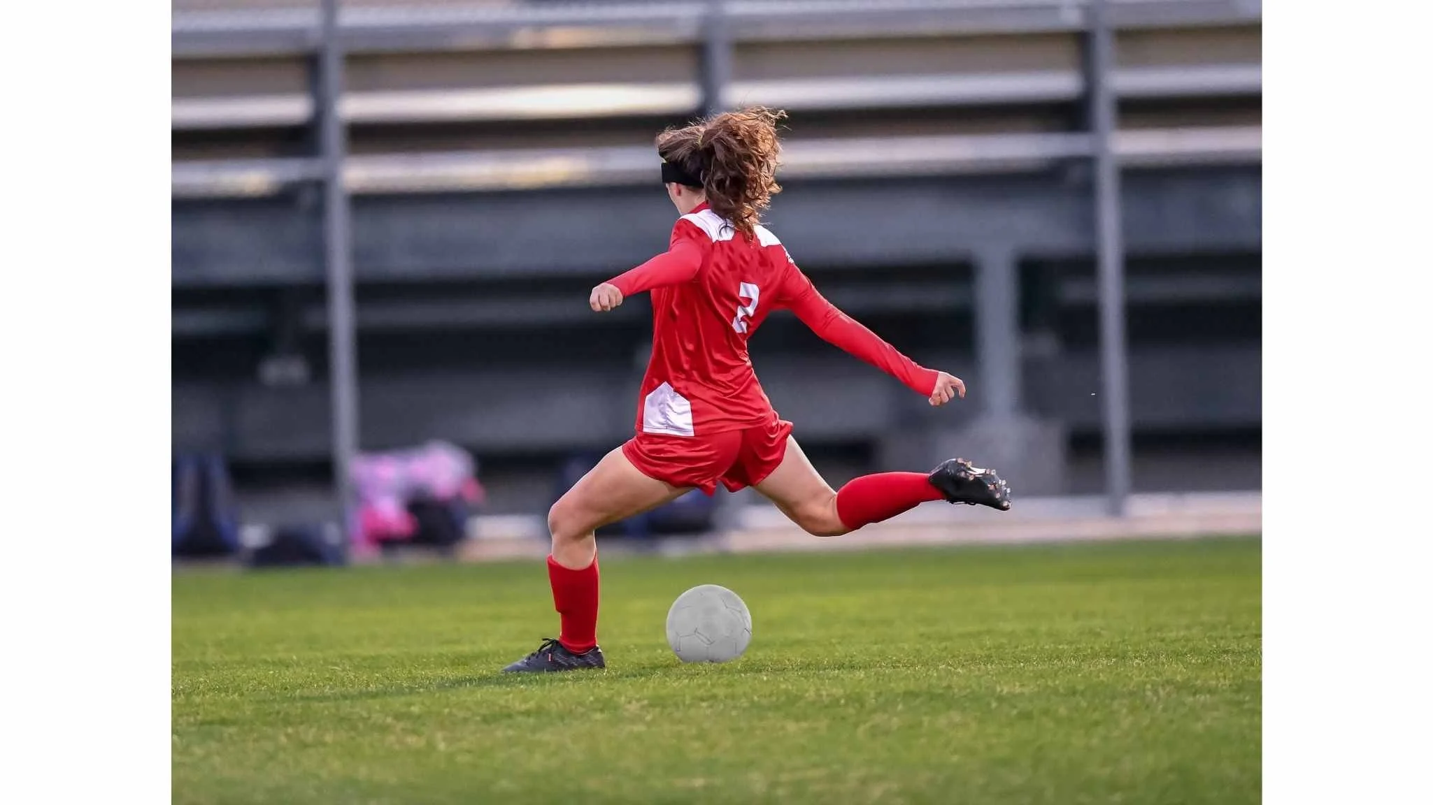 A female soccer player in a red uniform kicking a soccer ball on the field.