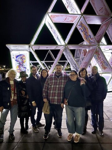 Group of people standing in front of a geometric light installation at night.