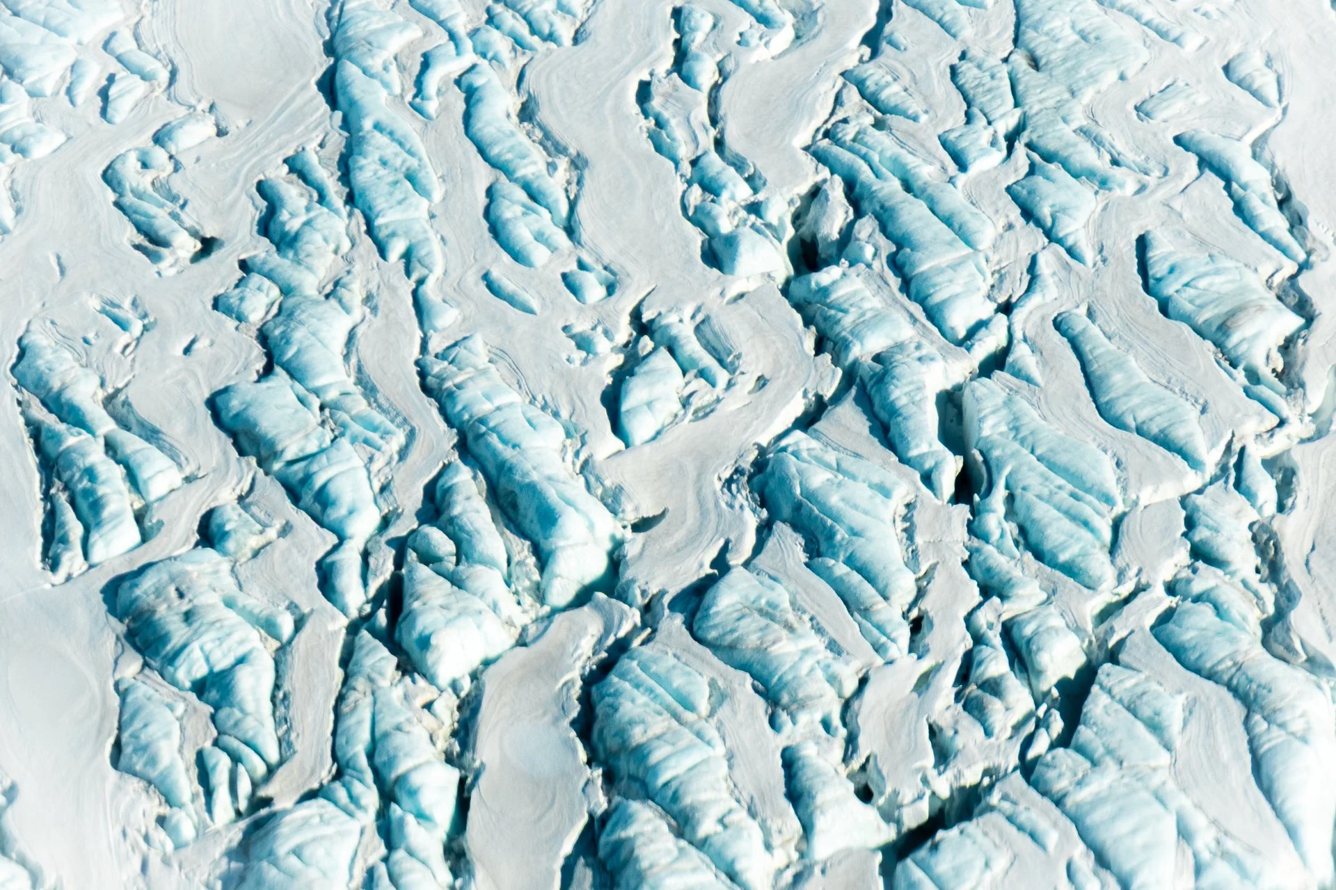 An aerial view of a glacier with deep crevasses and cracks in the ice, surrounded by snow.