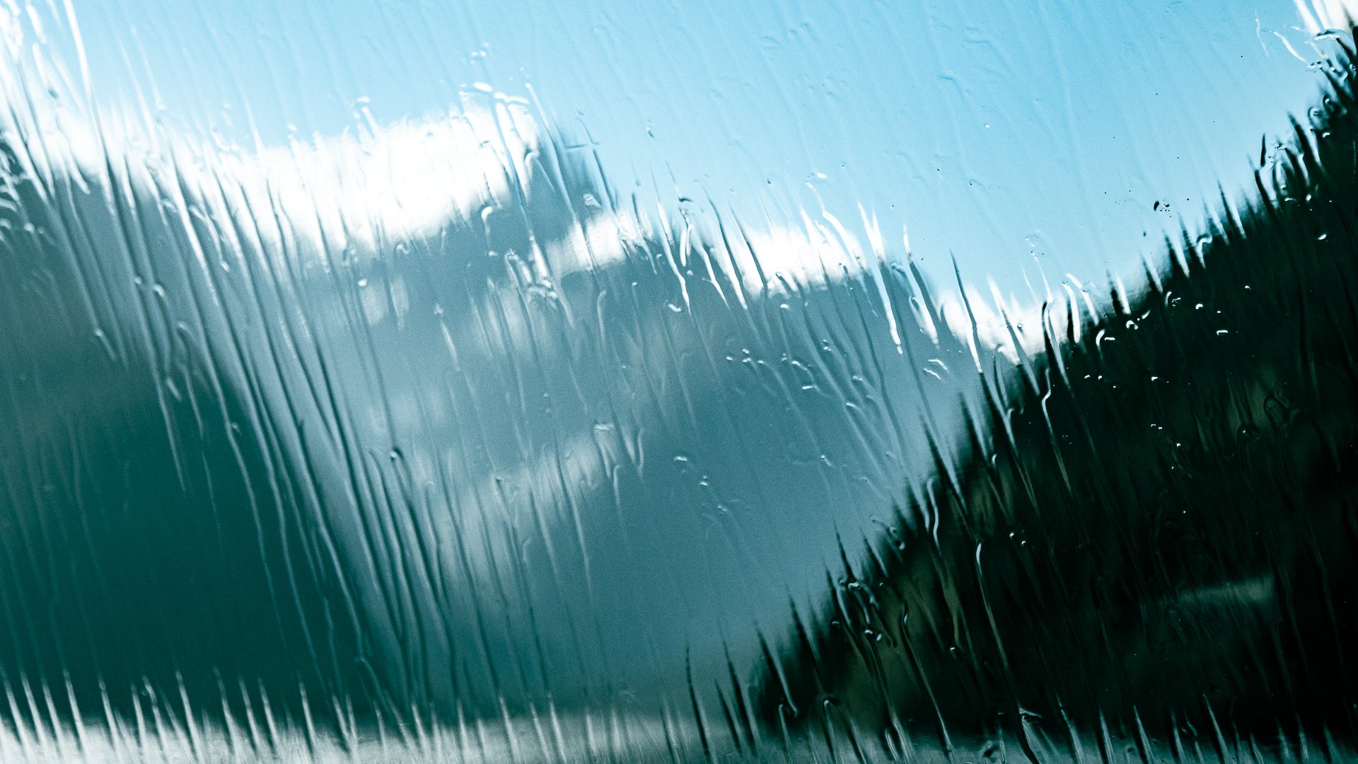 Close-up of a glass window with water droplets and streaks, slightly foggy or rainy weather outside.