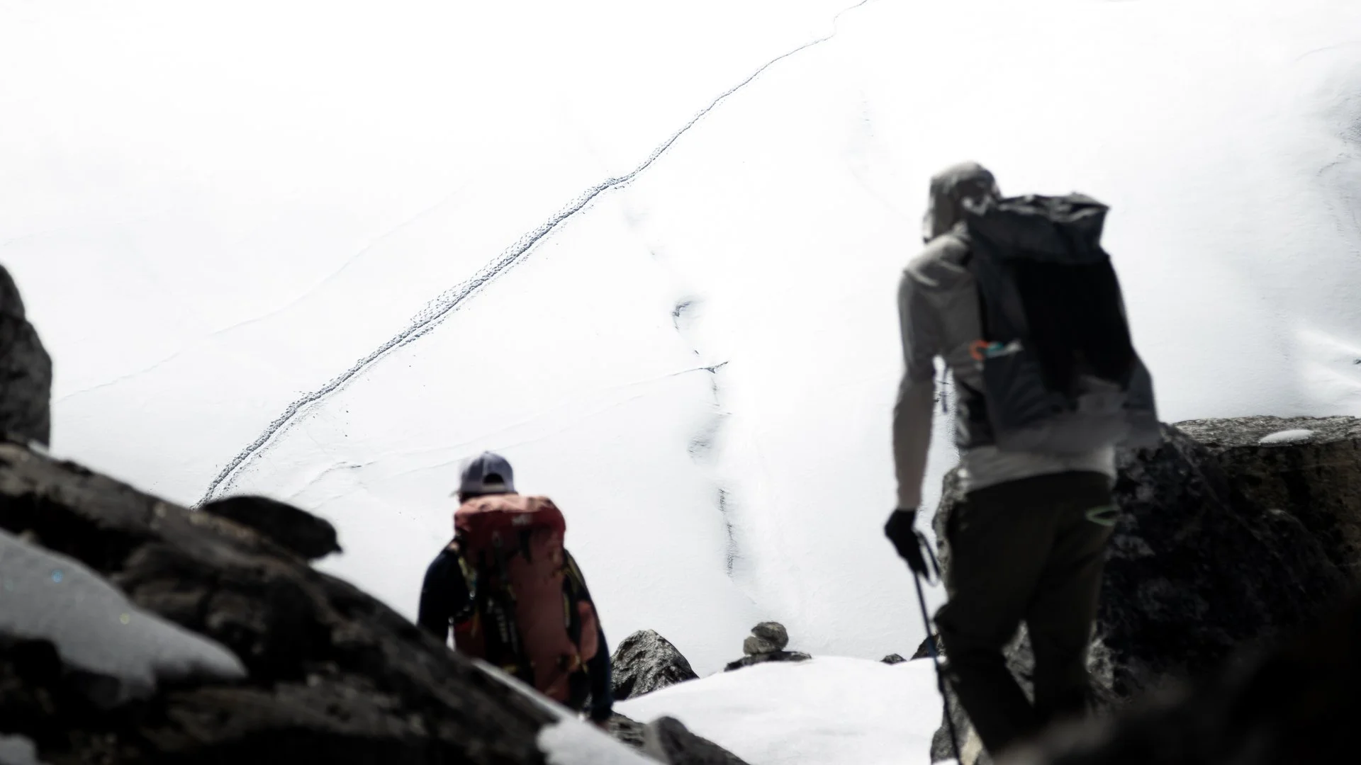 Group of hikers climbing a snow-covered mountain, seen from a low angle with rocks in the foreground.