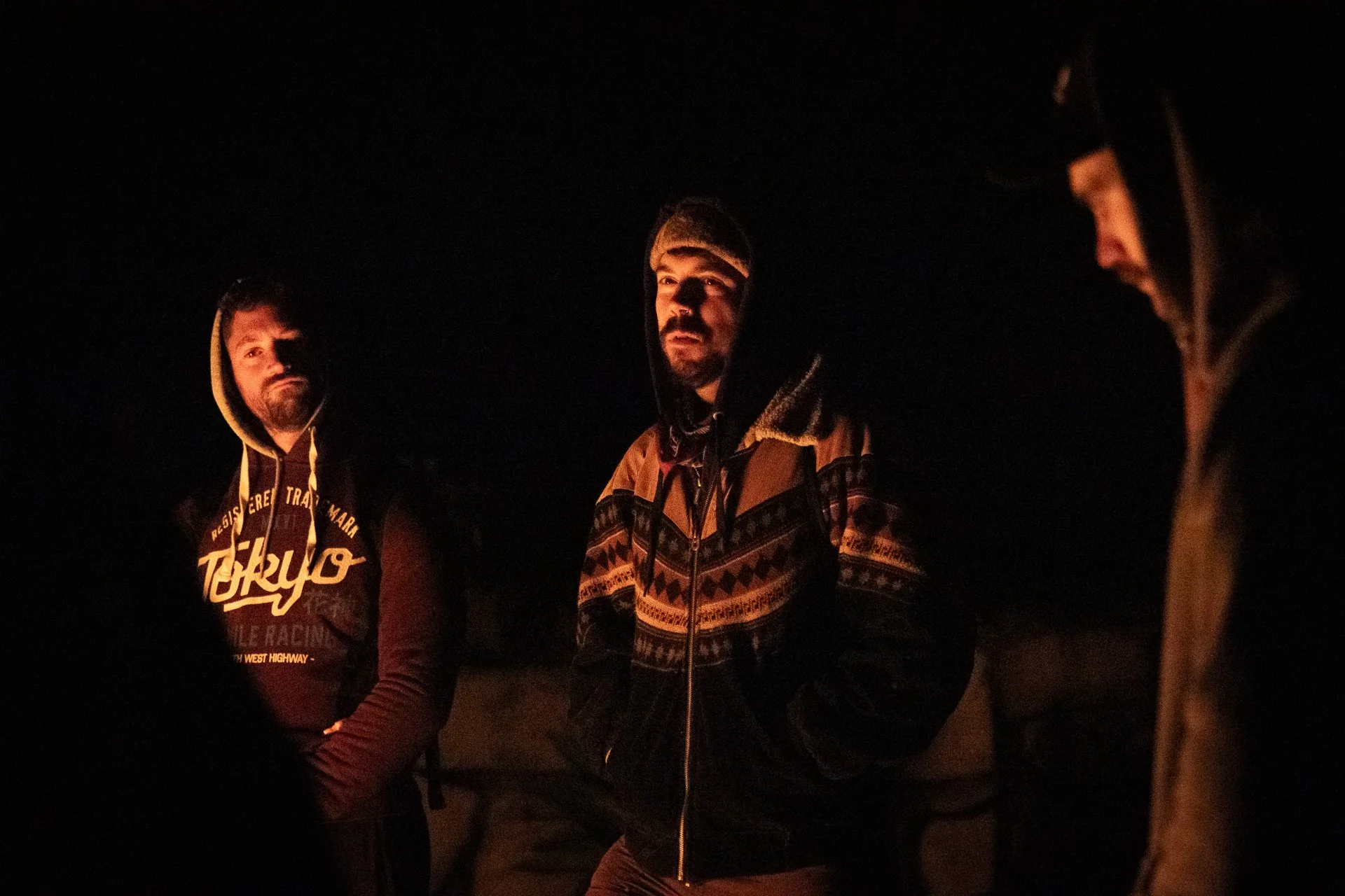 Three men standing around a campfire at night, illuminated by the firelight.