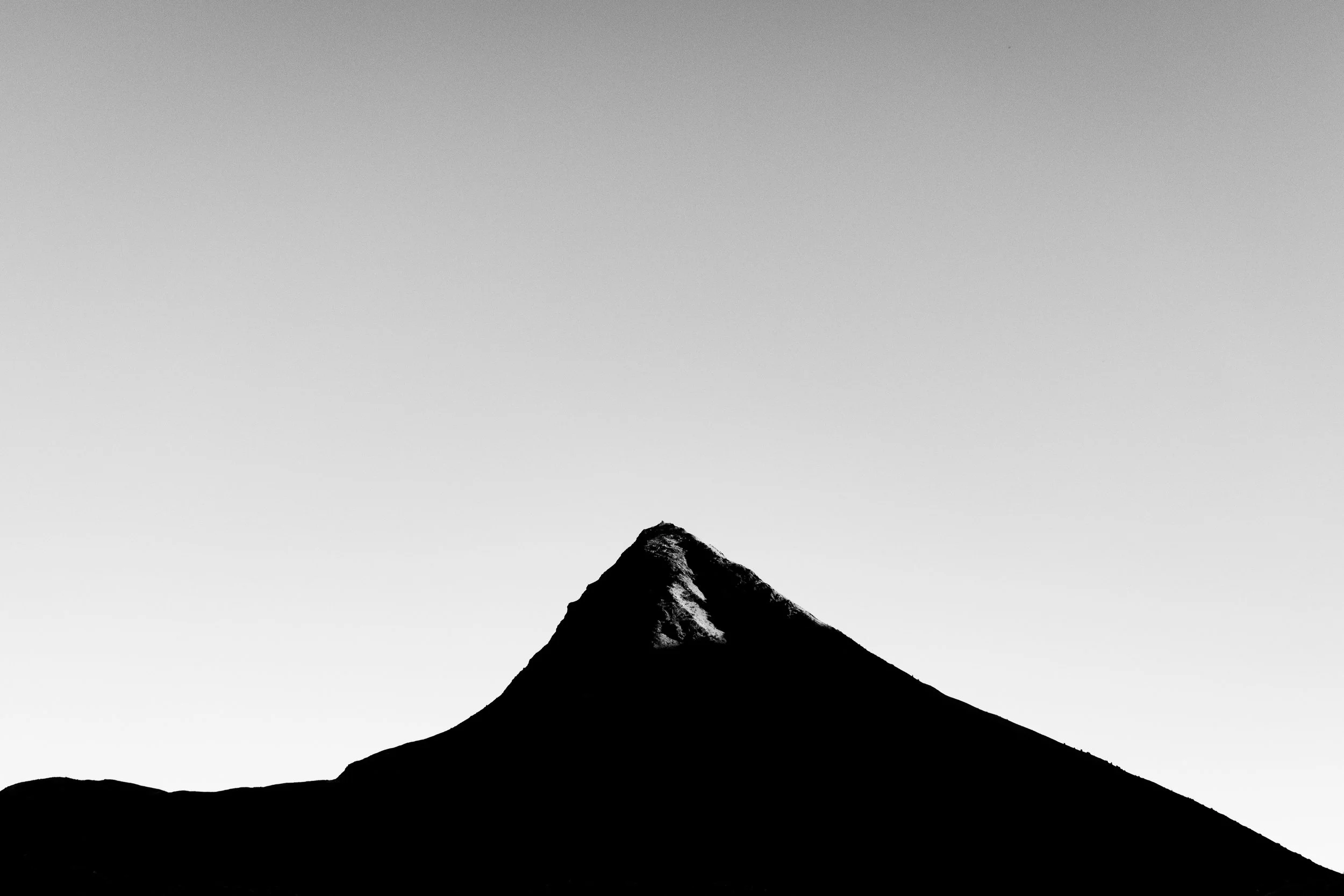 A black and white photo of a mountain peak with snow on one side, set against a gray sky.