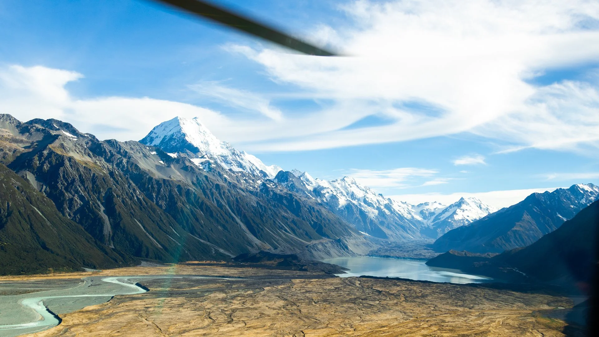 Snow-capped mountains, a river flowing through a valley, and a partly cloudy sky.