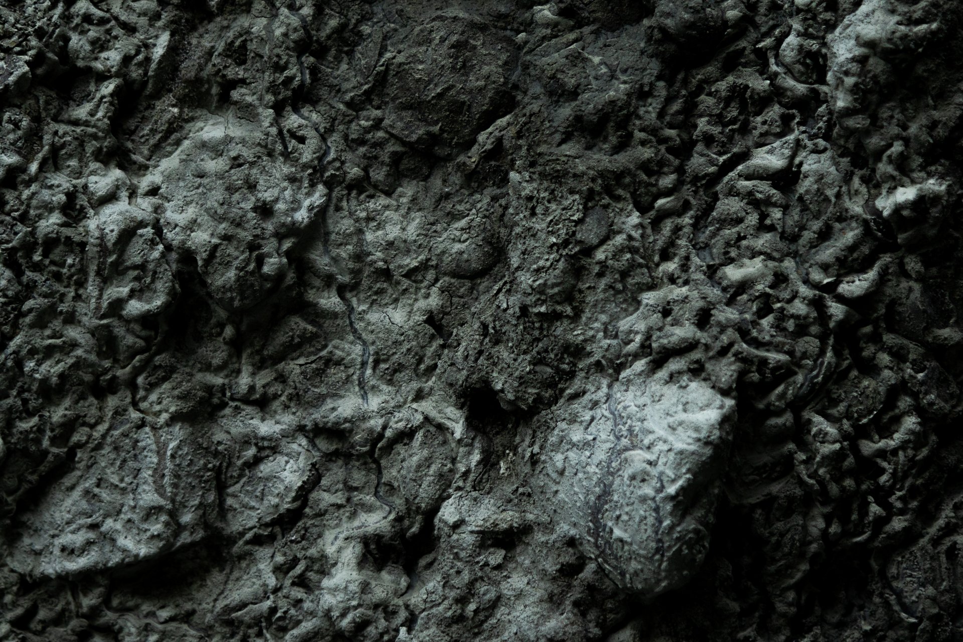 Close-up view of rough, gray, volcanic rock surface with cracks and uneven texture.