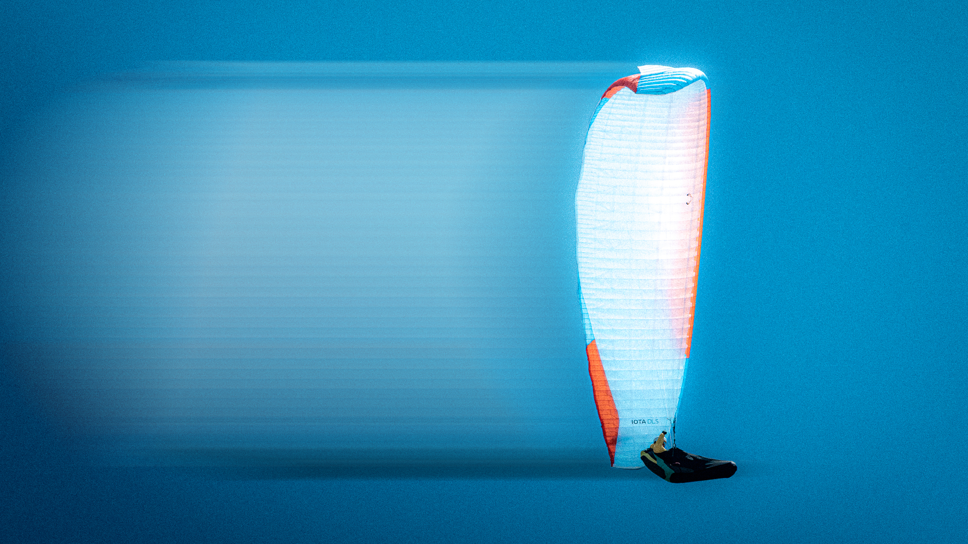 A person paragliding with a red, white, and blue parachute against a clear blue sky.