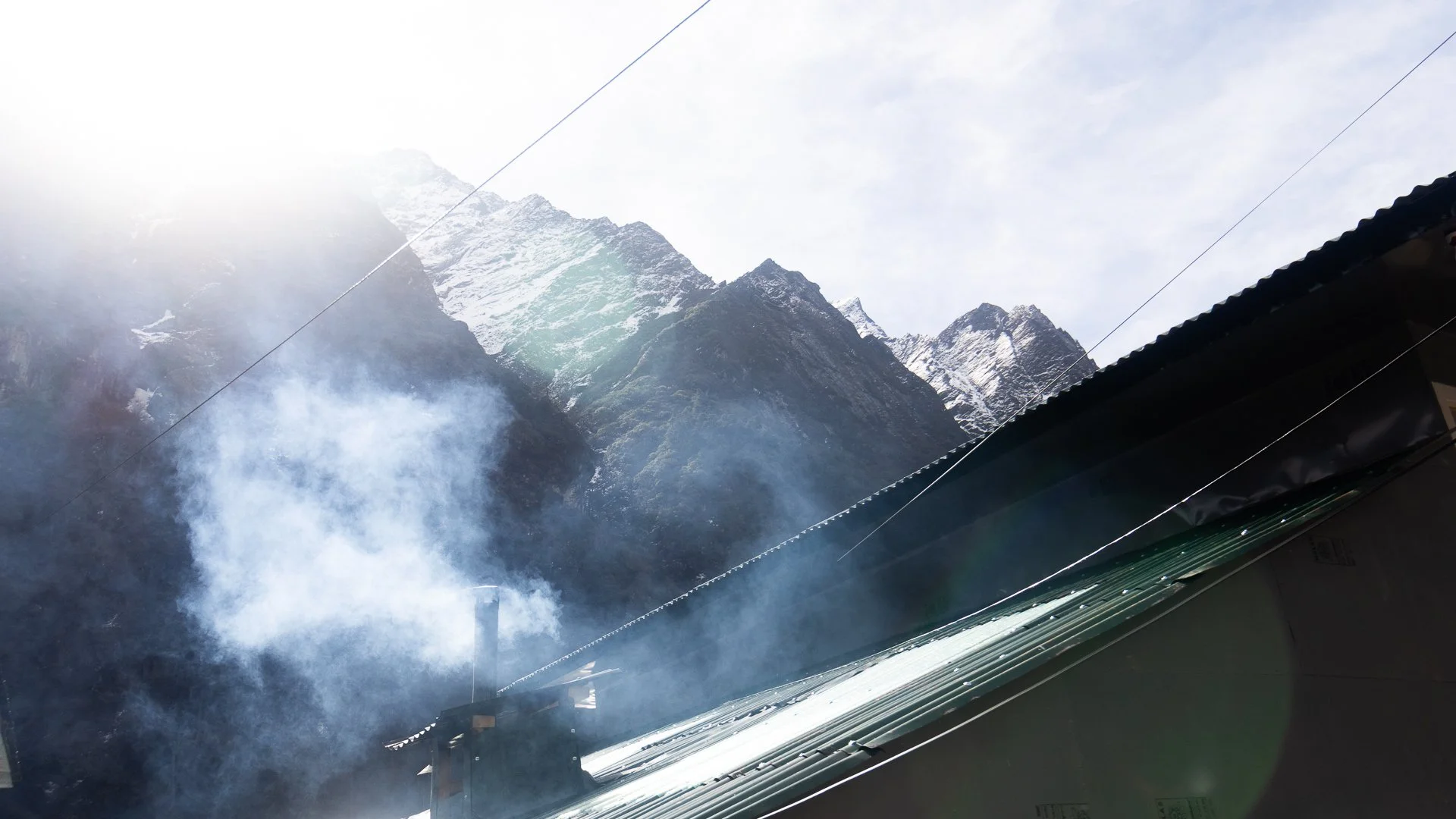 Snow-capped mountain range seen through a partially open window with smoke or fog in the foreground.