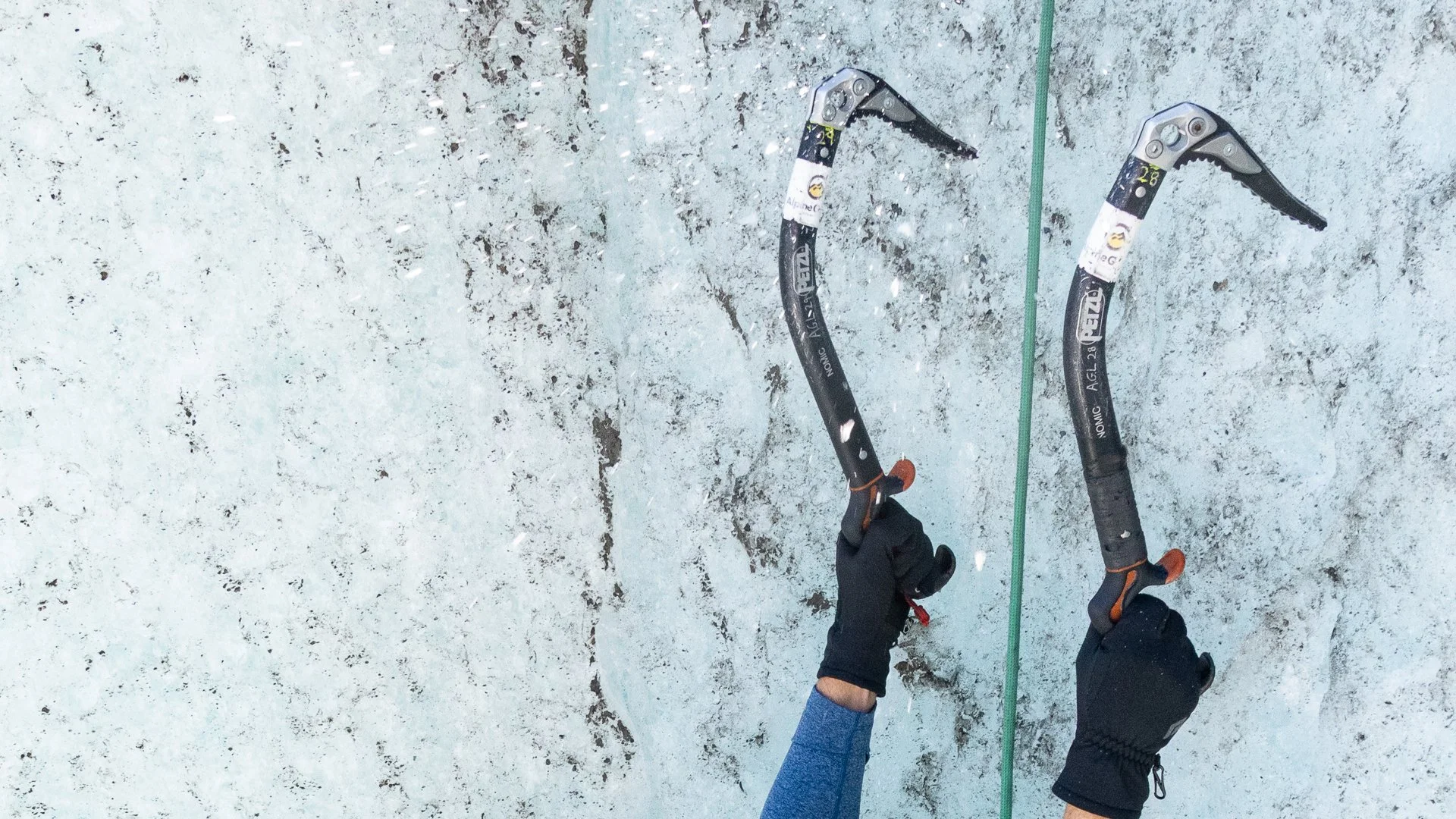 View from a person's perspective holding two ice axes on a snowy, icy surface during a winter mountain climb.